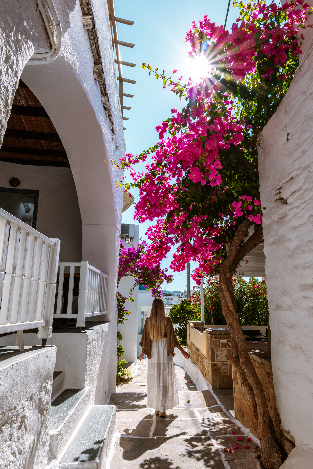 Woman walking in Ios Chora village under pink bougainvillea flowers, Greece