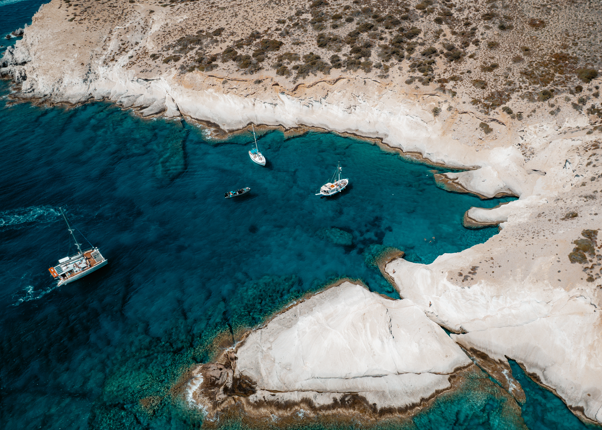 Drone view of crystal clear water, boats, and white rock formations in Antiparos, Greece