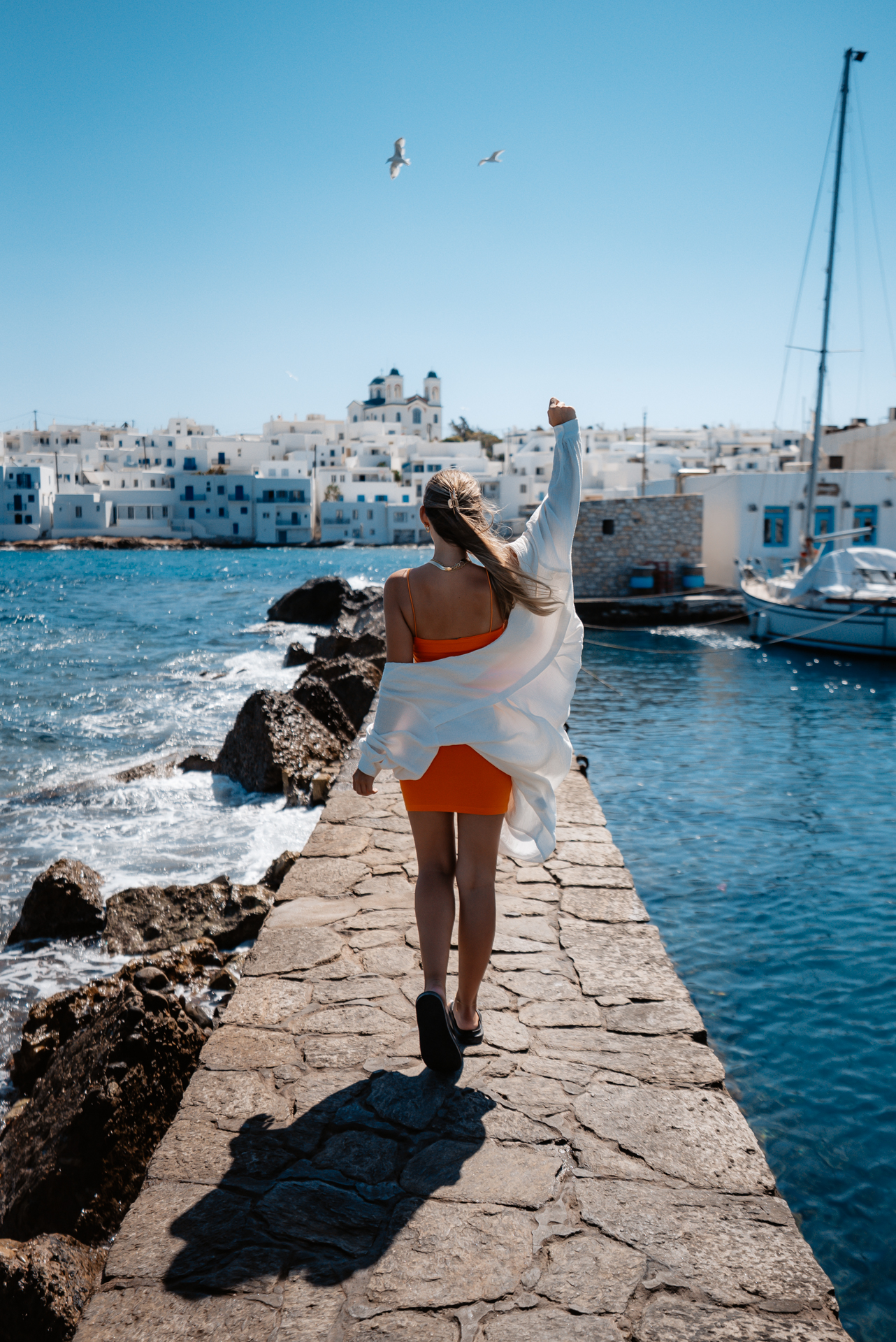 Woman walking on harbor pier in Paros with white houses and sea view