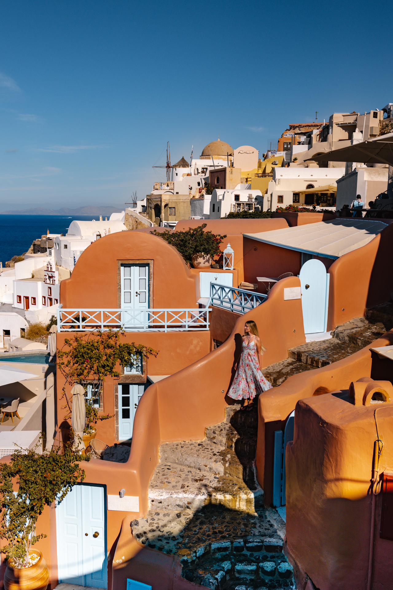 Woman walking through colorful houses in Oia Santorini with sea view