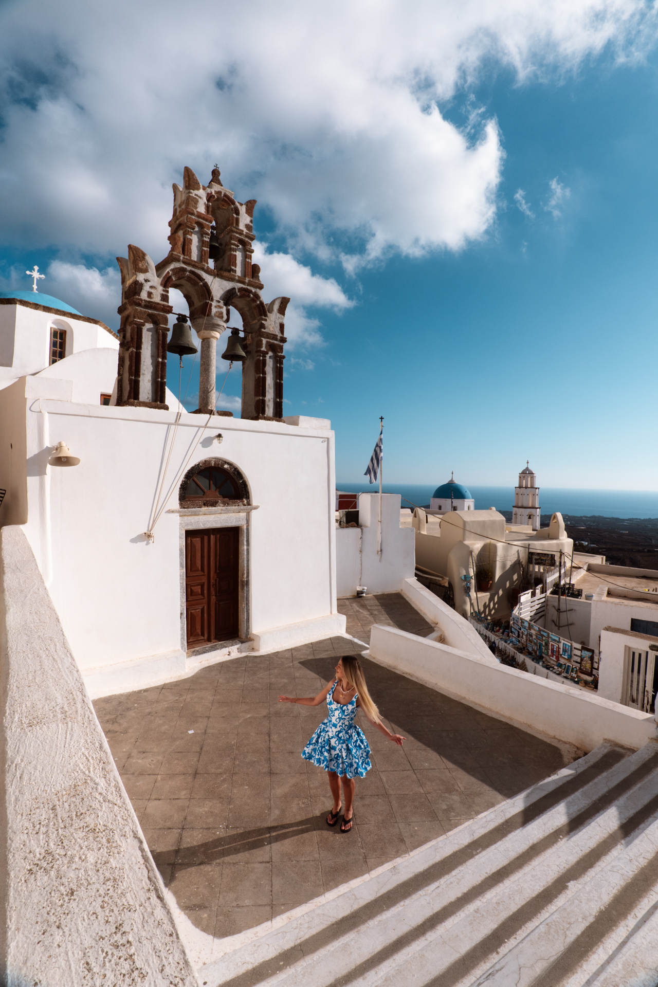 Woman at Santorini church with blue dome and bell tower overlooking the island