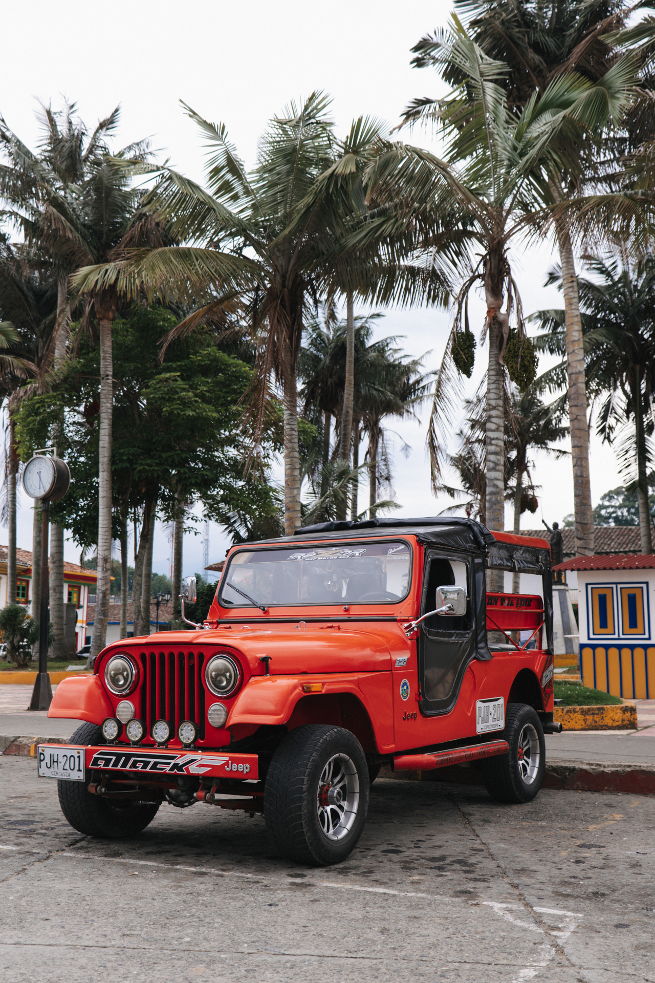 Classic red Jeep in Salento town square with palm trees and colorful buildings