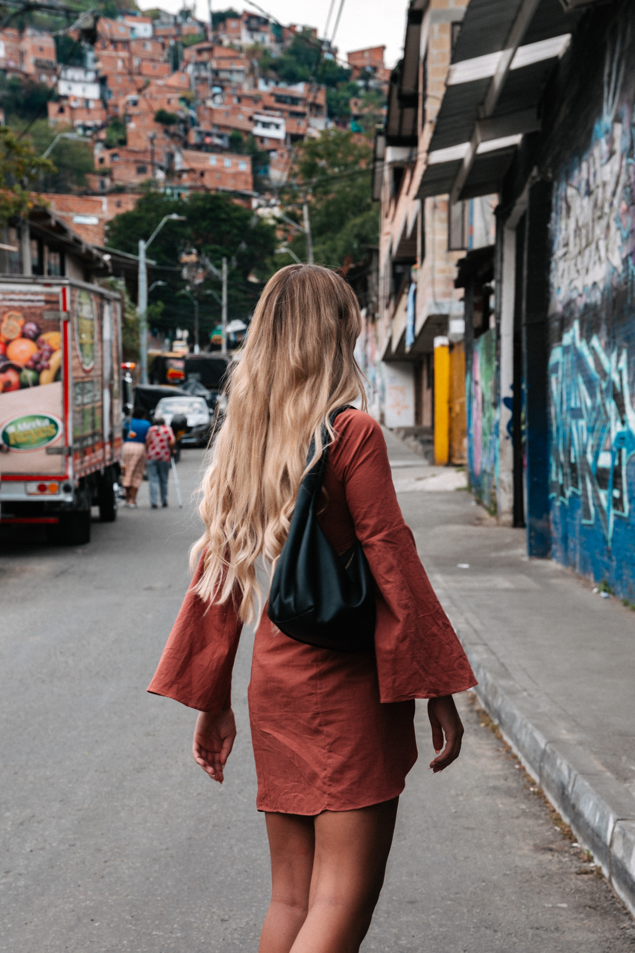 Woman walking Medellin street with hillside homes and urban life