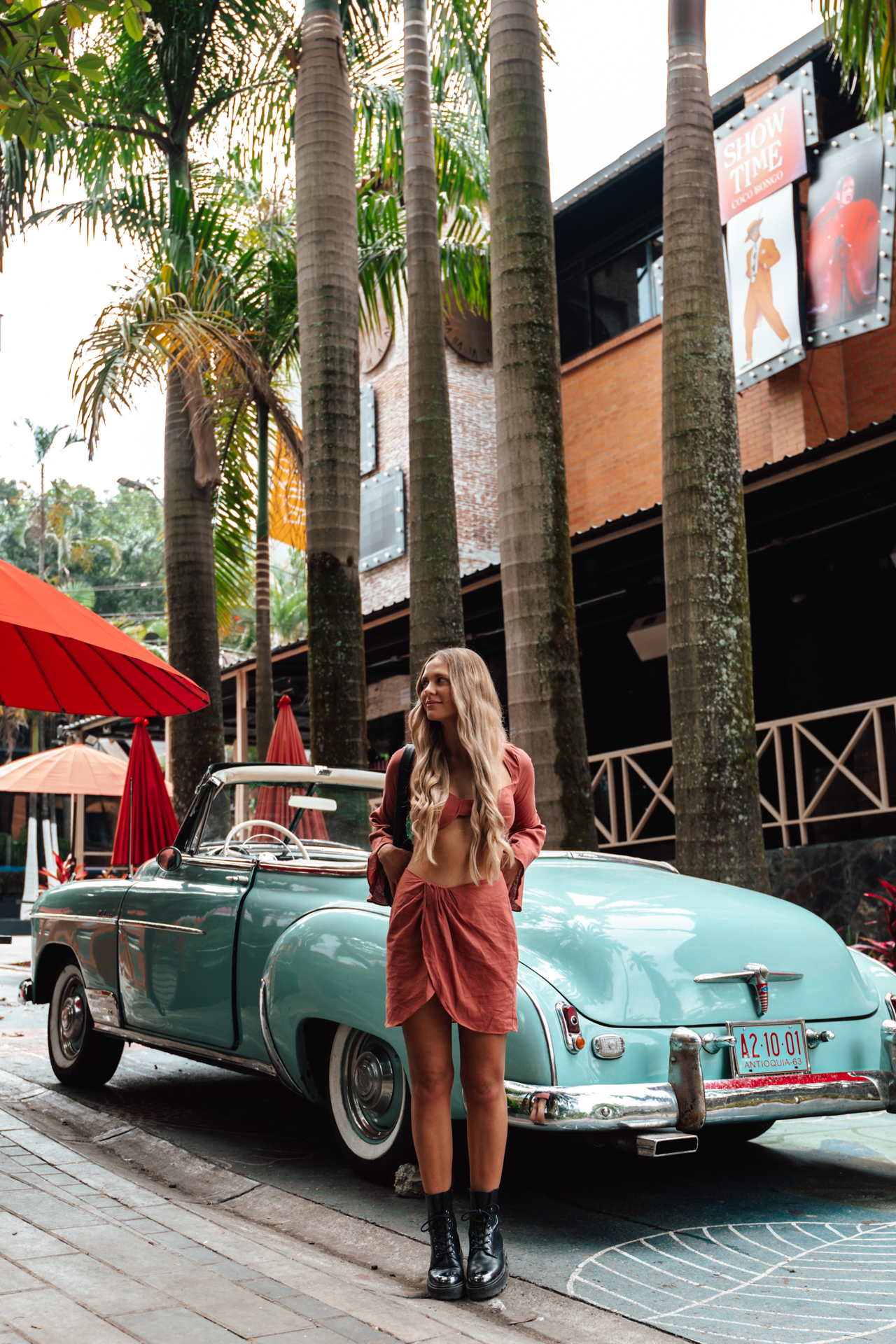 Woman by vintage car in Medellin with palm trees and colorful vibe