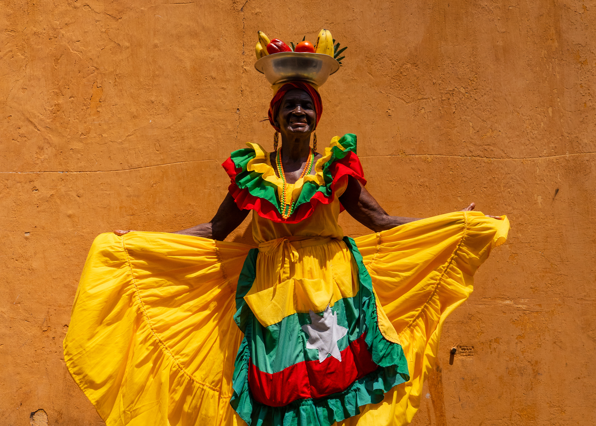 Cartagena woman in traditional dress with fruit basket posing against colorful wall