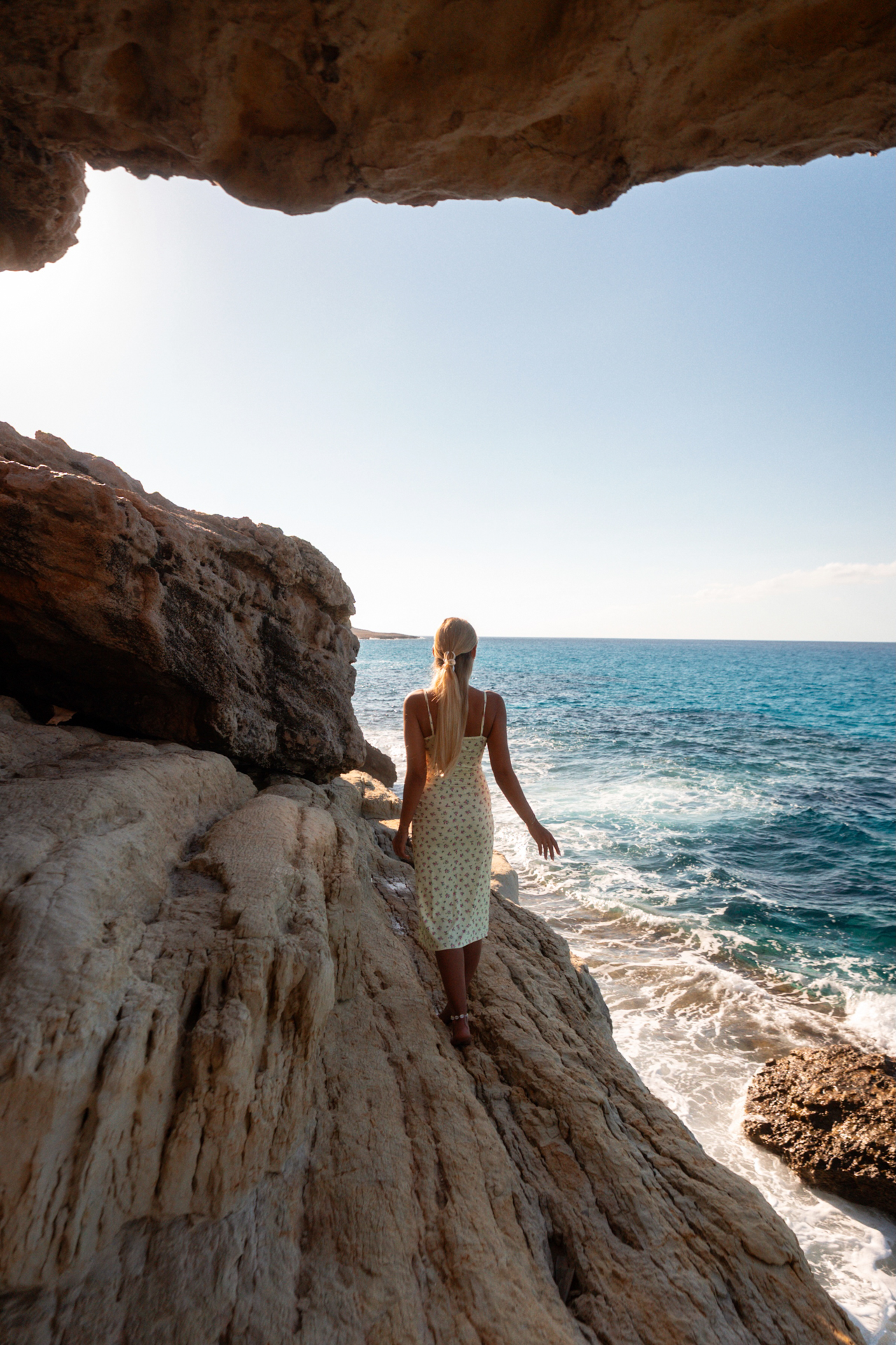 Woman walking along rocky cliffs overlooking the sea at Cape Greco, Cyprus
