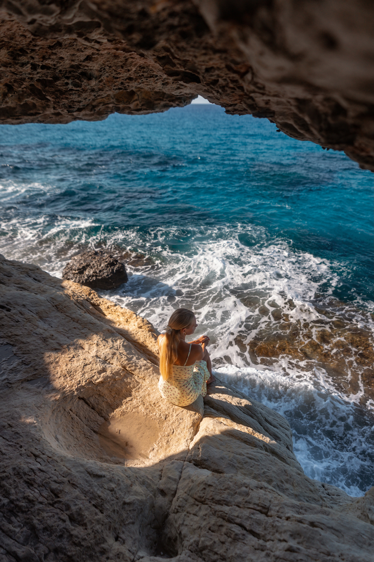Woman sitting on rocky cliff above turquoise sea, Cyprus