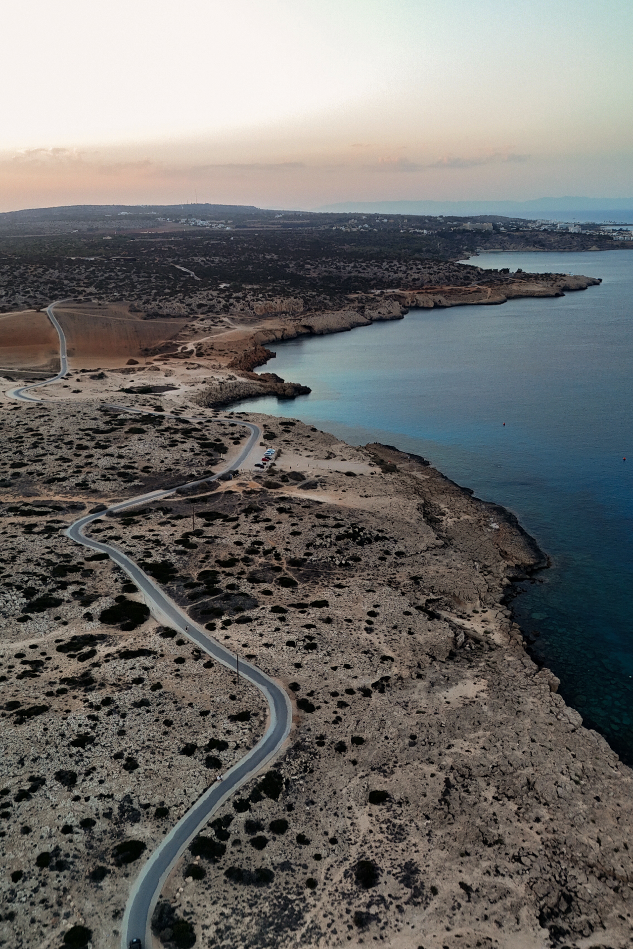 Aerial view of rugged coastline and winding road at sunset, Cyprus at Cape Greco