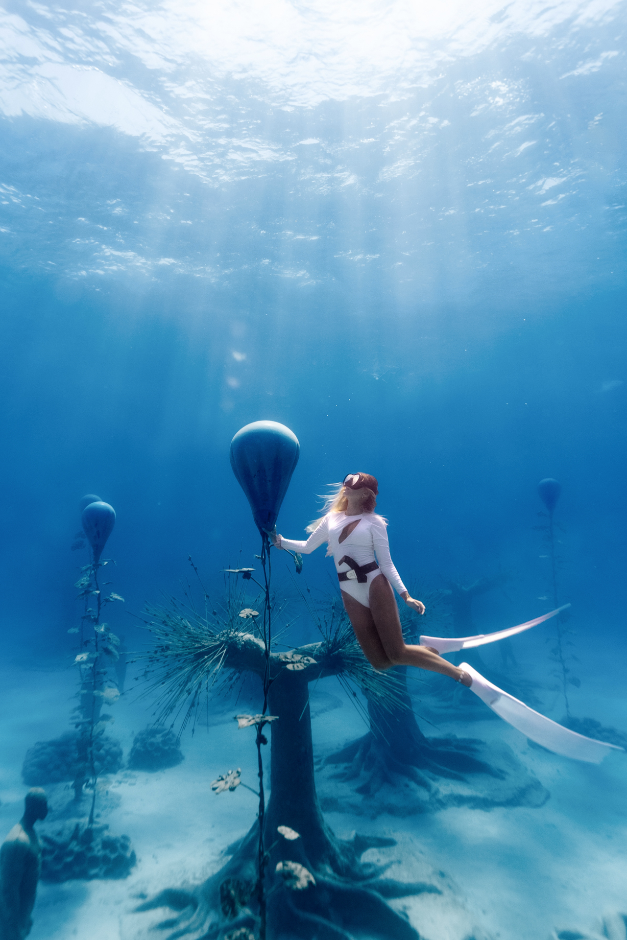 Freediver gliding past submerged sculptures and trees at MUSAN museum