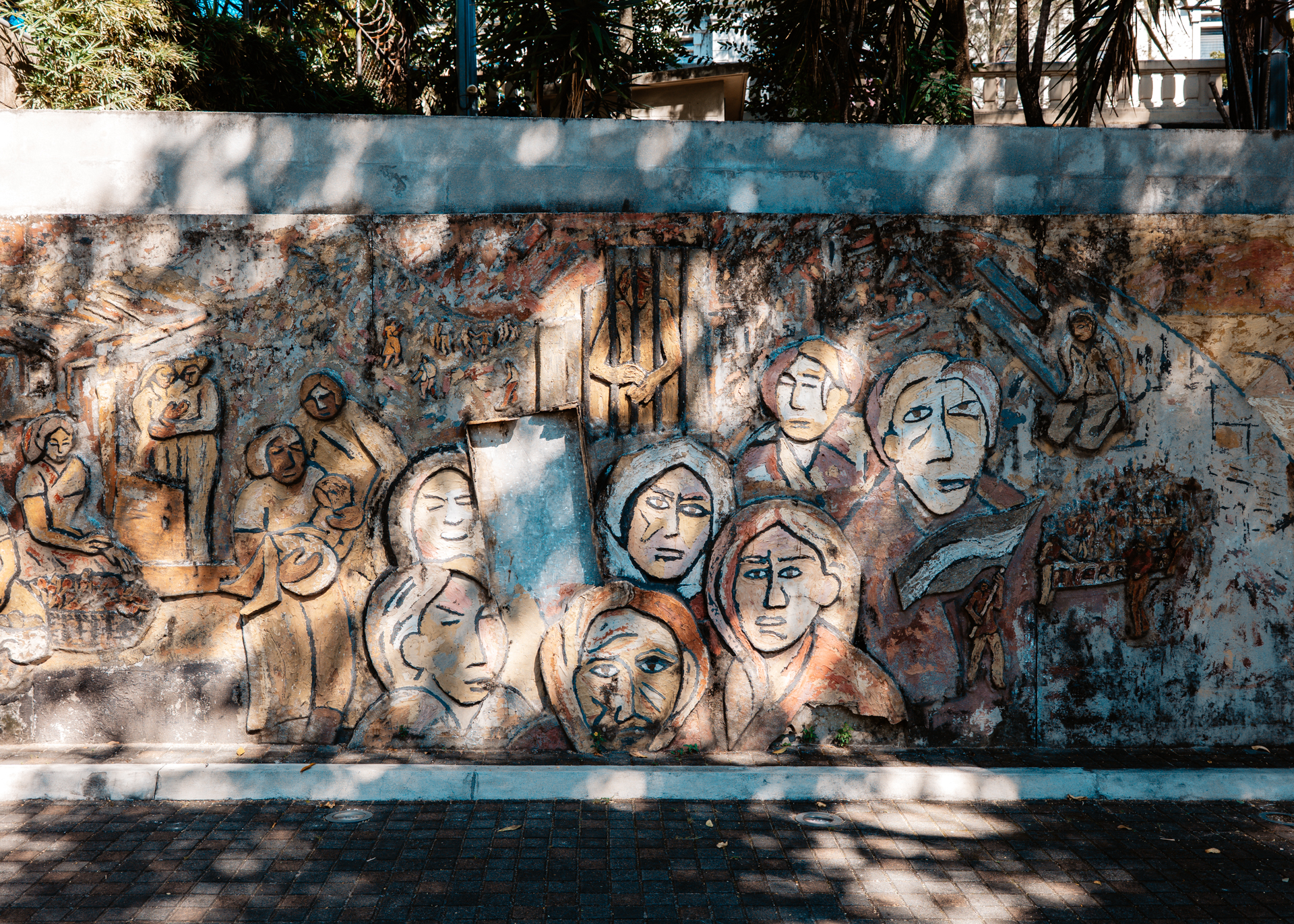Weathered mural of faces and scenes at Monumento a la Memoria y la Verdad in San Salvador