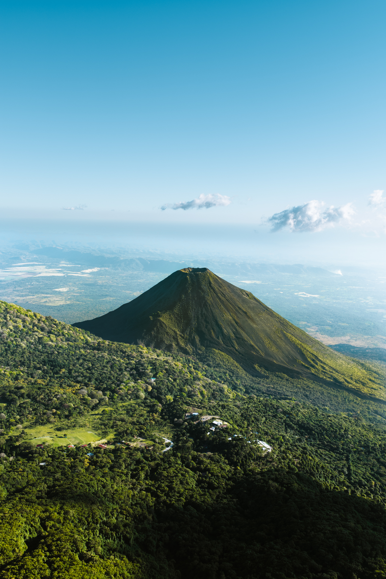 Aerial view of aIzalco Volcano rising above dense forest under a clear blue sky