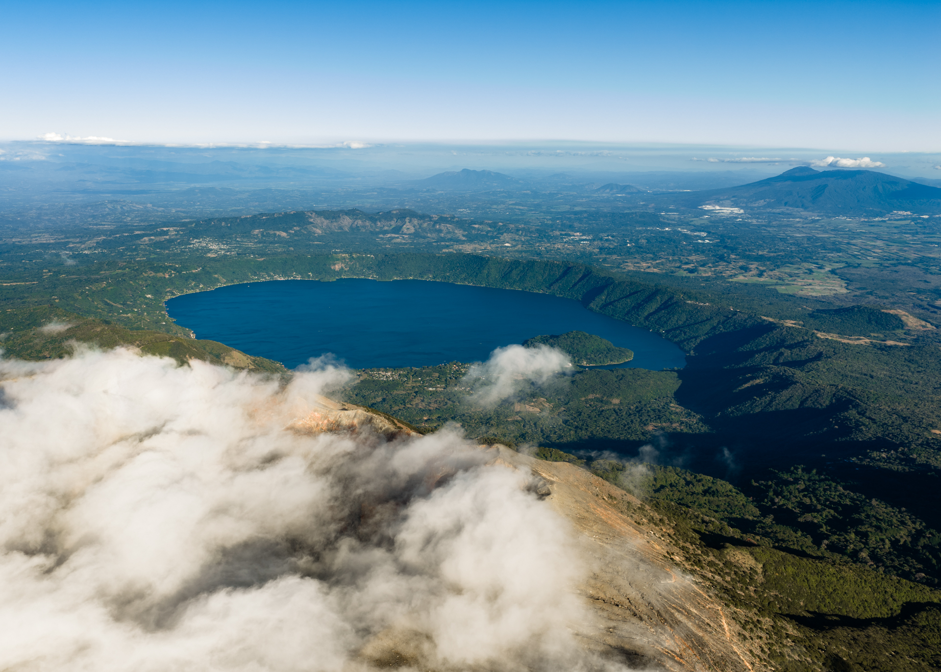 Aerial view of Lake Coatepeque in a volcanic caldera surrounded by lush green hills and clouds