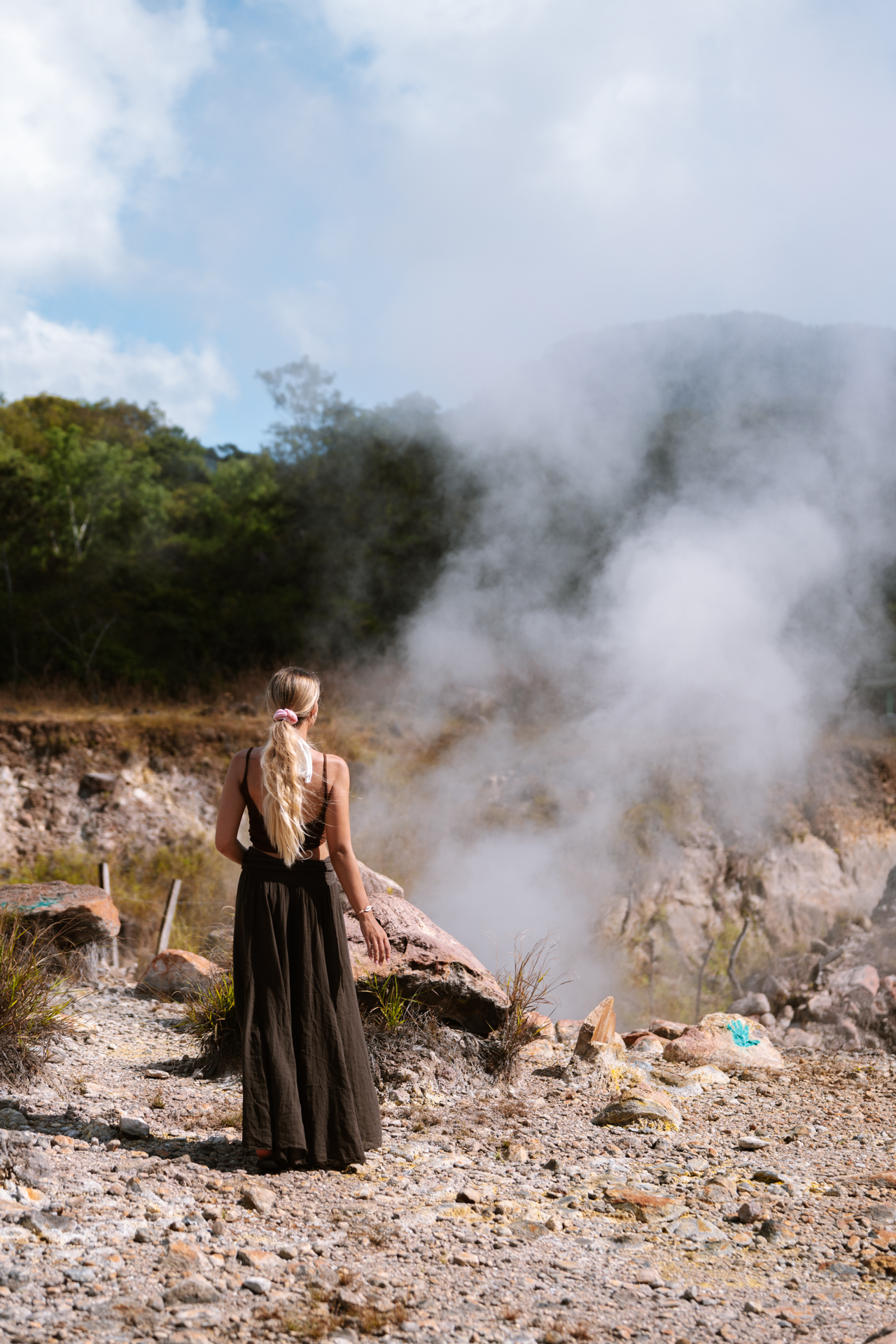 Woman at Los Ausoles geothermal area with steam rising from hot springs in El Salvador
