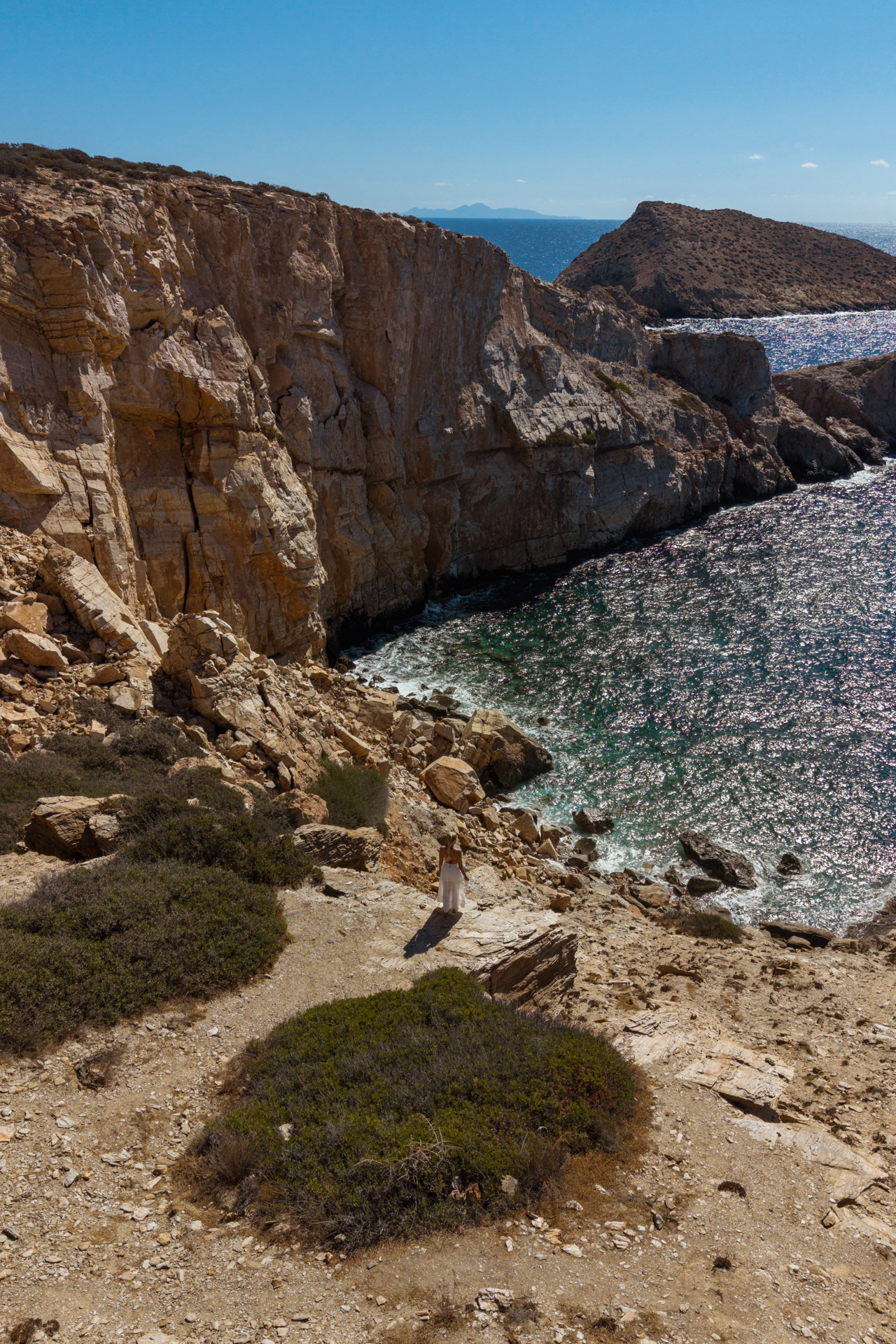 Rocky cliffs at Never Bay, Ios with woman overlooking turquoise sea