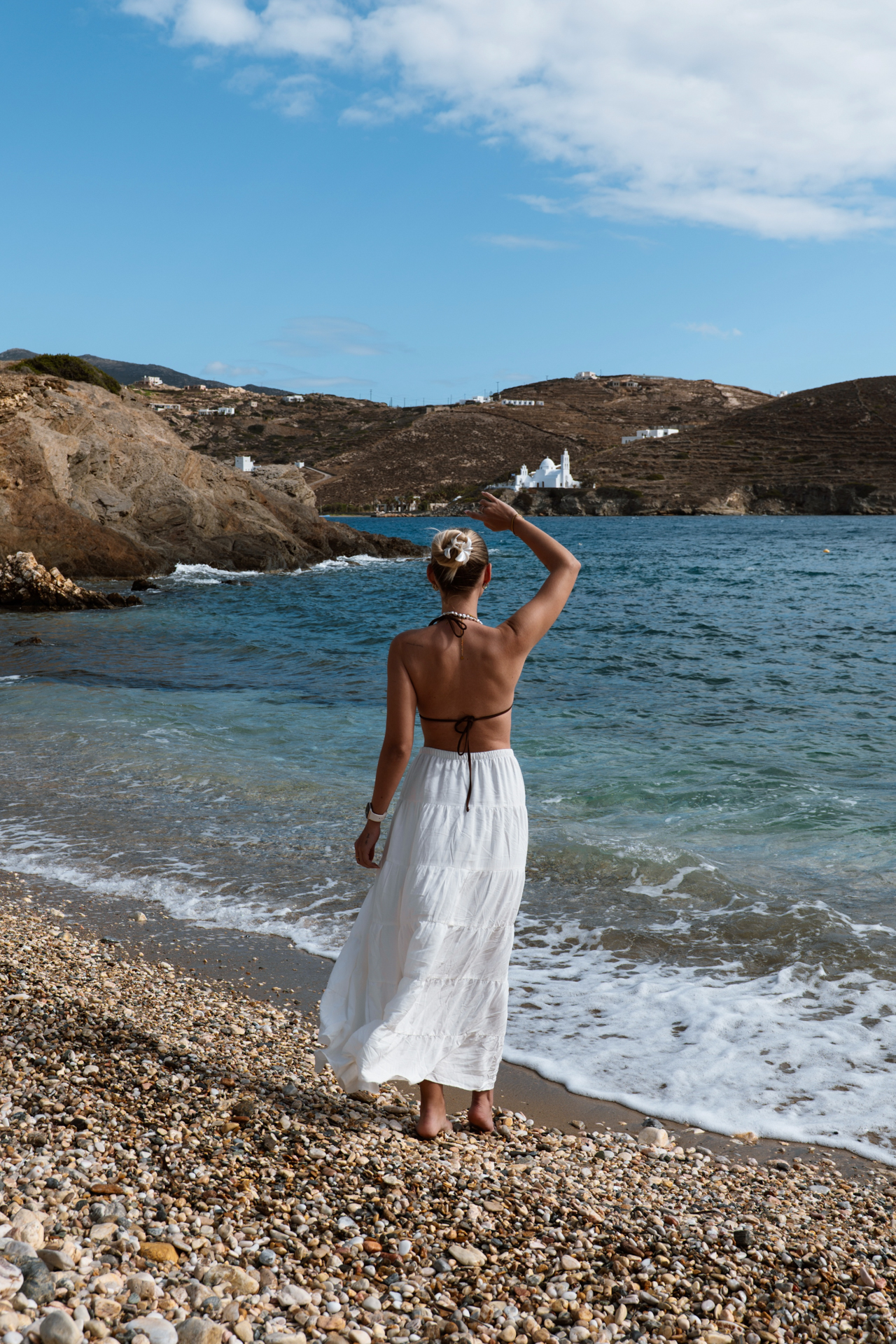 Woman standing on pebble shore at Tzamaria Beach, Ios with waves and hills