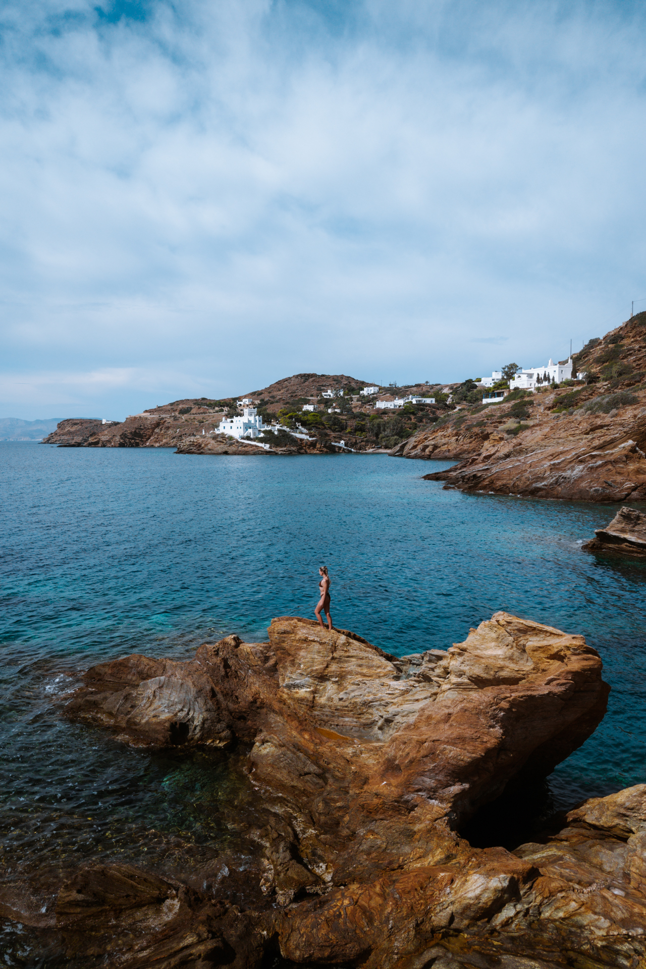 Woman standing on rocks by the sea near Mylopotas Beach, Ios