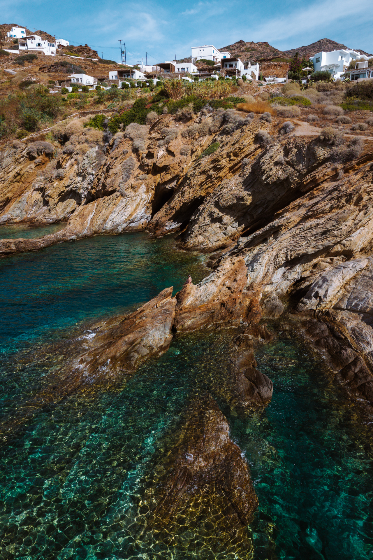 Rocky cove with clear turquoise water on Ios with hillside houses above