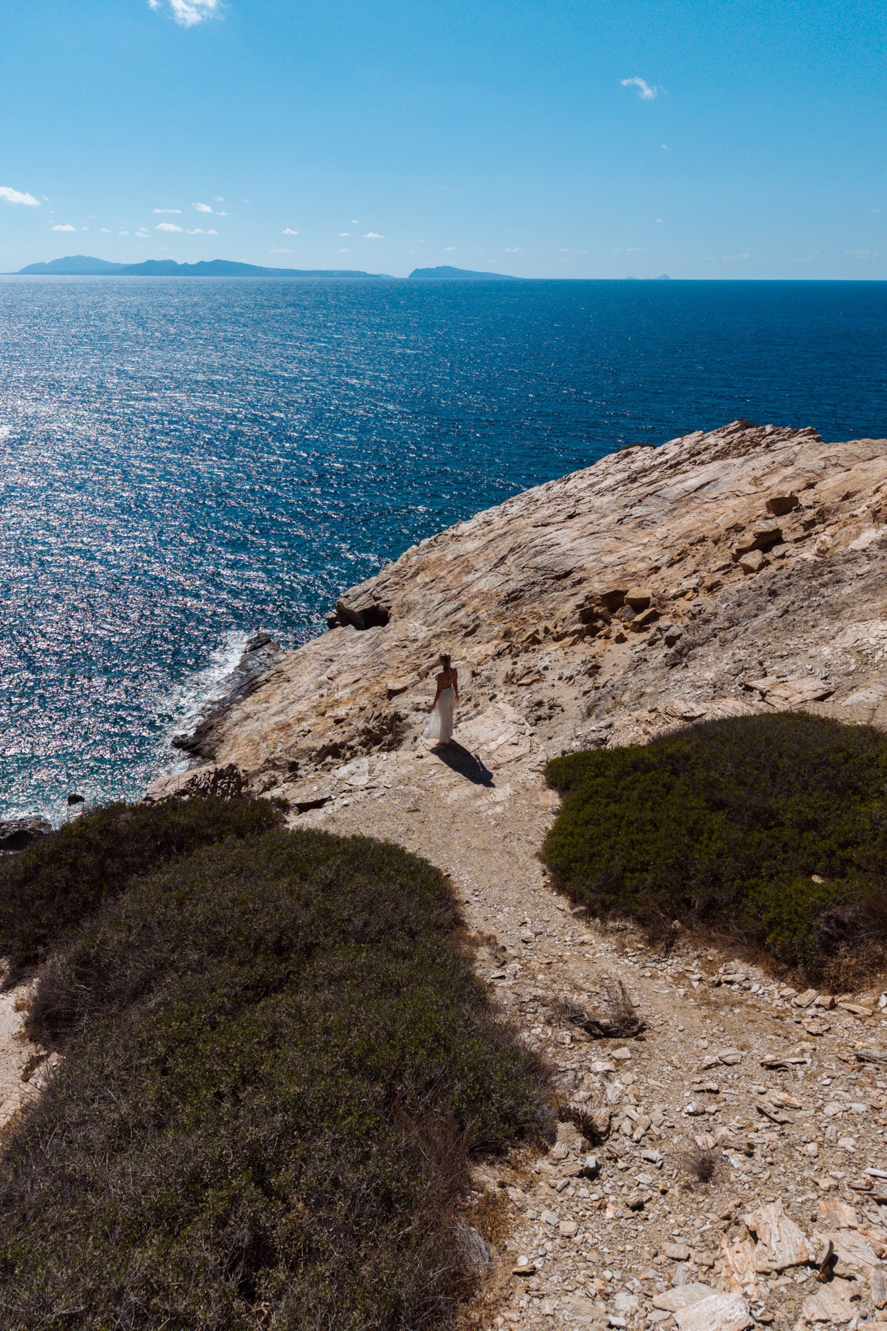 Coastal trail at Never Bay, Ios with woman walking above deep blue water