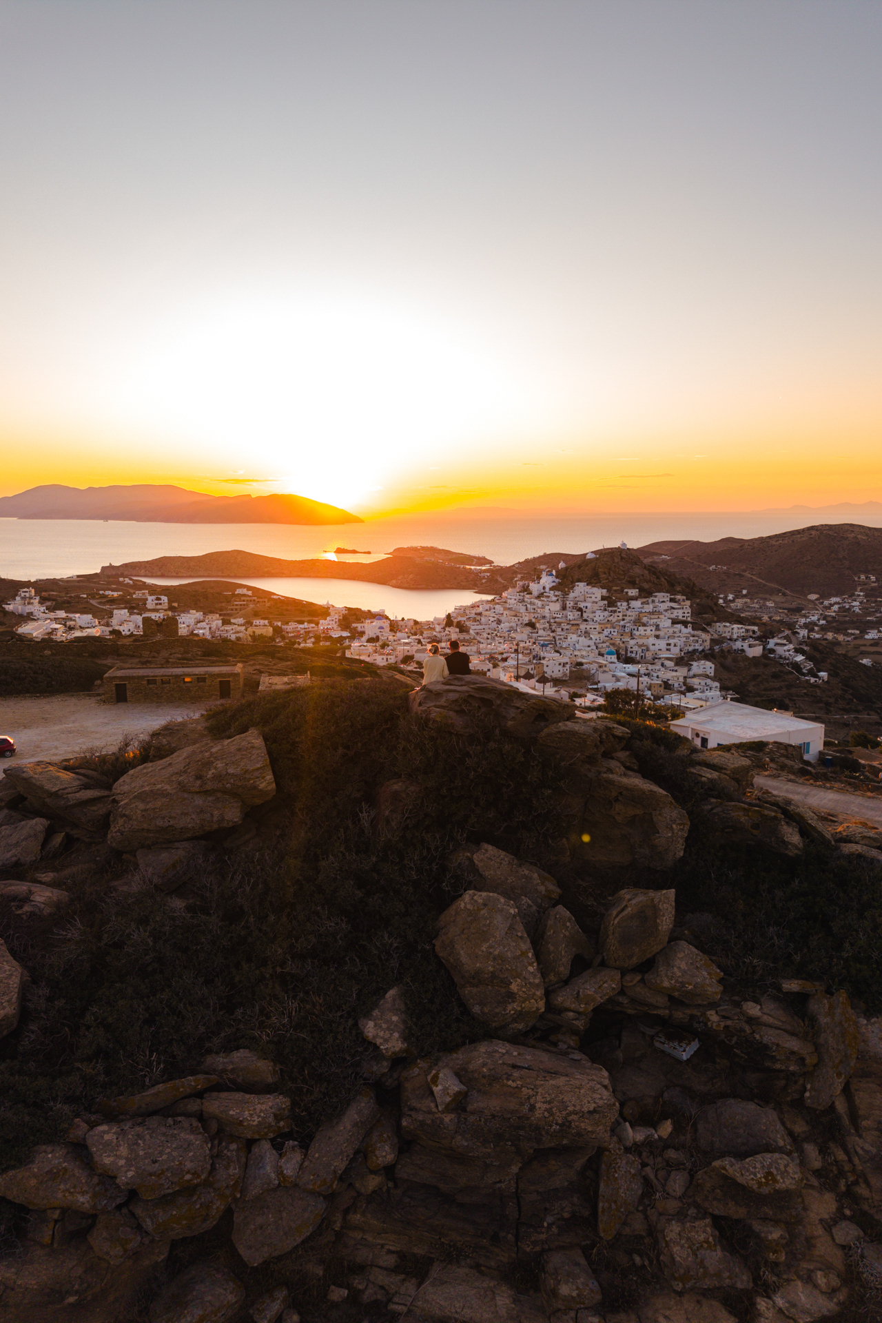 Sunset view over Chora, Ios with couple on rocks and golden sea horizon