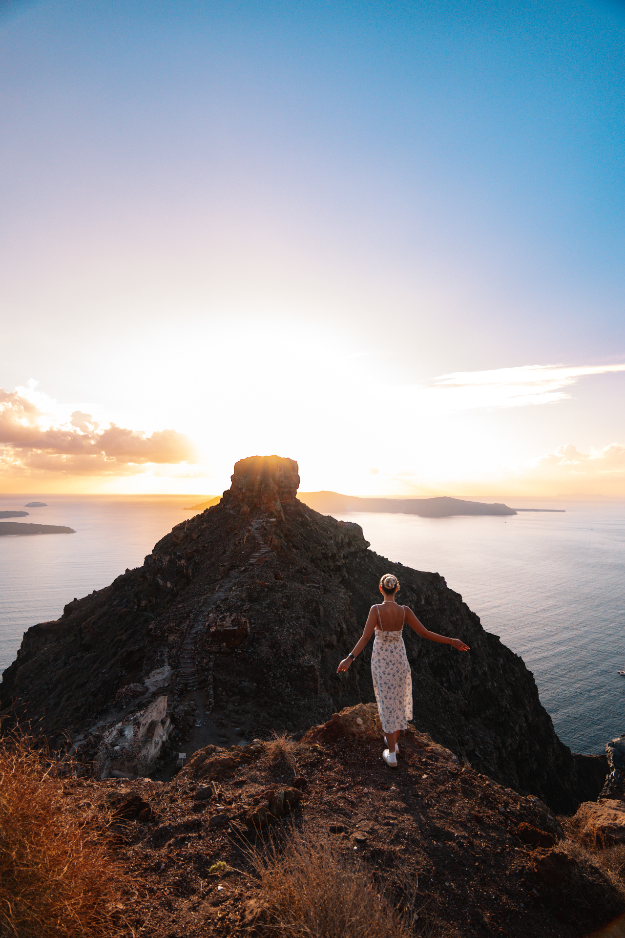 Woman at Skaros Rock Santorini at sunset overlooking caldera and Aegean Sea