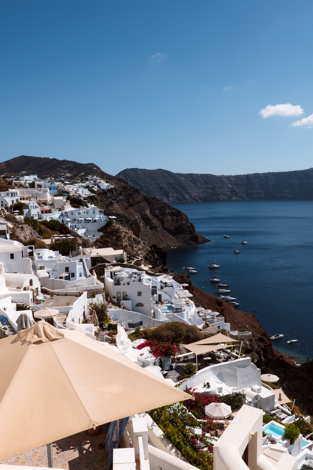 Oia Santorini cliffside with white houses, caldera view and boats in Aegean Sea