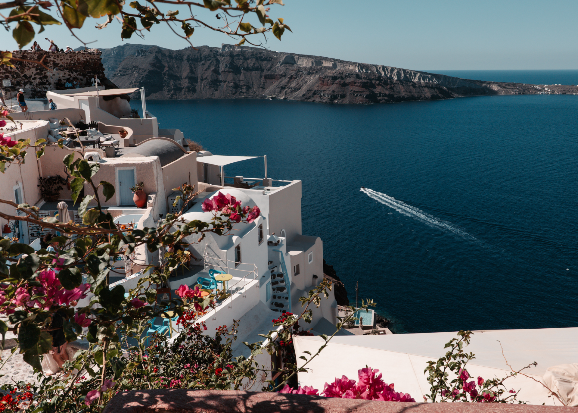 Santorini caldera view with white houses, bougainvillea flowers and boat on Aegean Sea