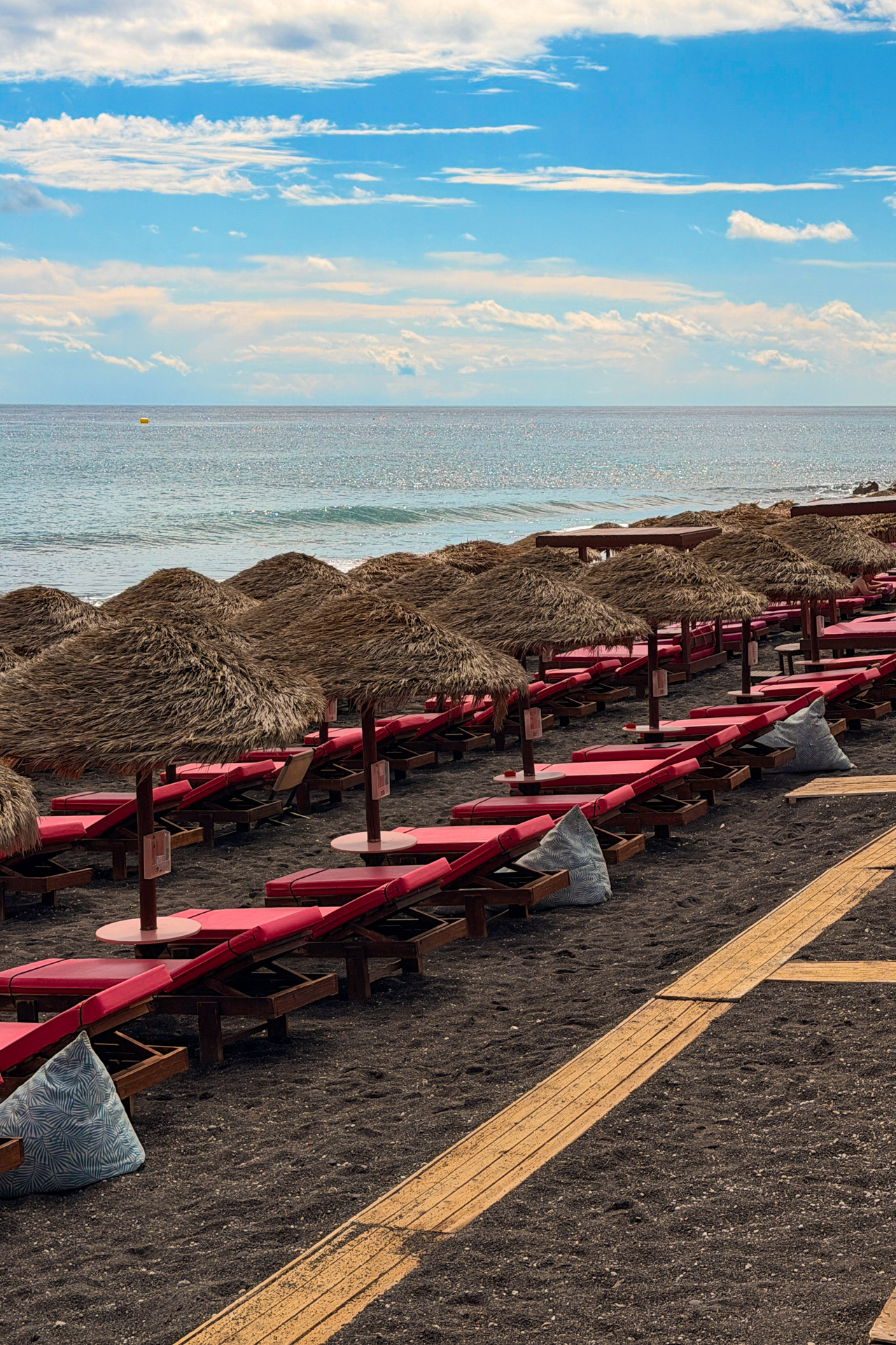 Perissa Beach Santorini with sunbeds, straw umbrellas and black volcanic sand