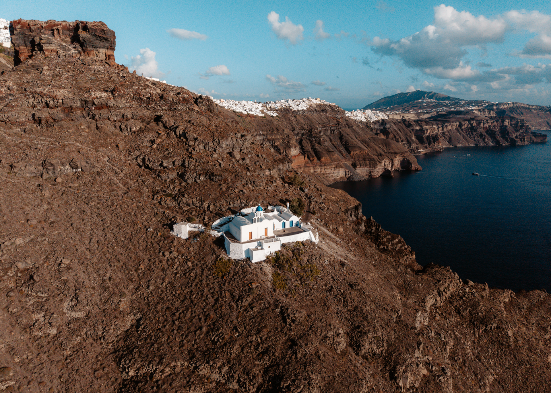 Santorini cliffside chapel with blue dome overlooking caldera and volcanic landscape