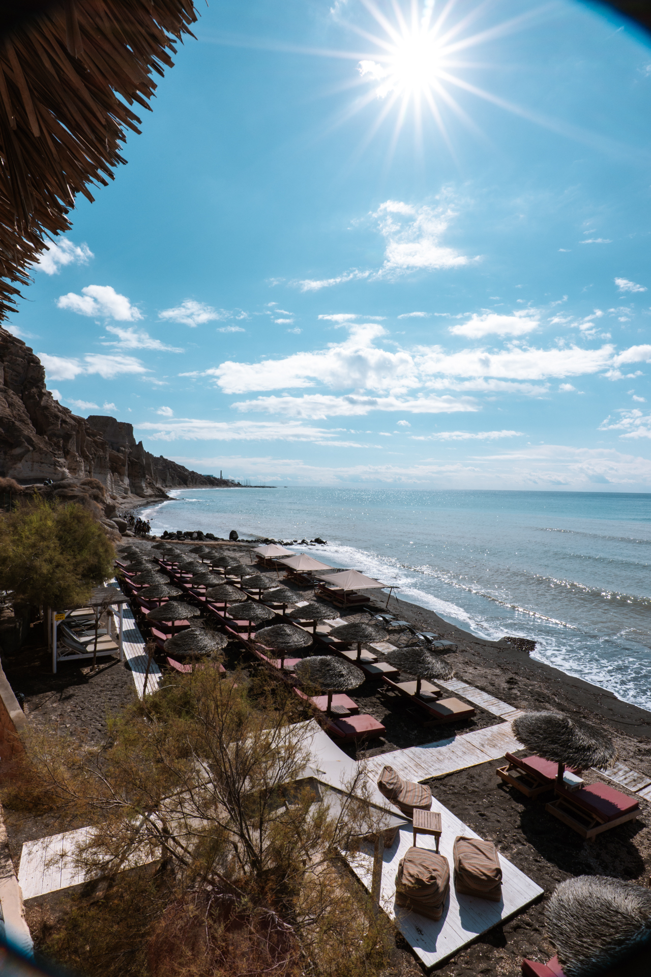 Eros Beach Santorini with sunbeds, umbrellas and black sand under bright sun