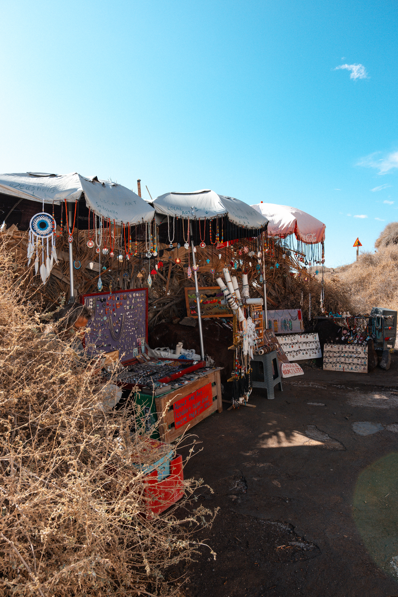 Souvenir stall at Santorini Red Beach with handmade jewelry and local art under sunshade