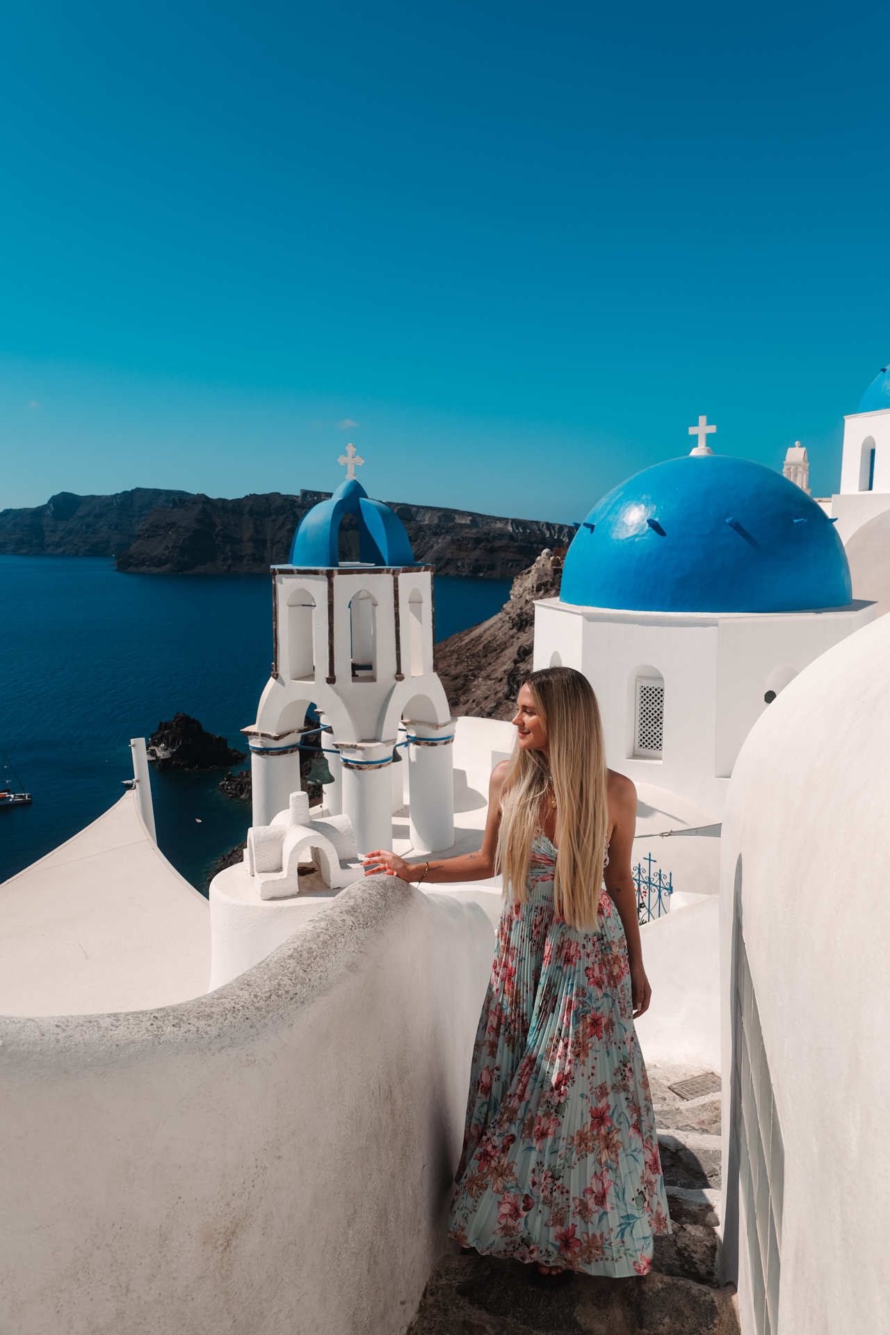 Woman in Oia Santorini by blue dome church overlooking caldera and sea