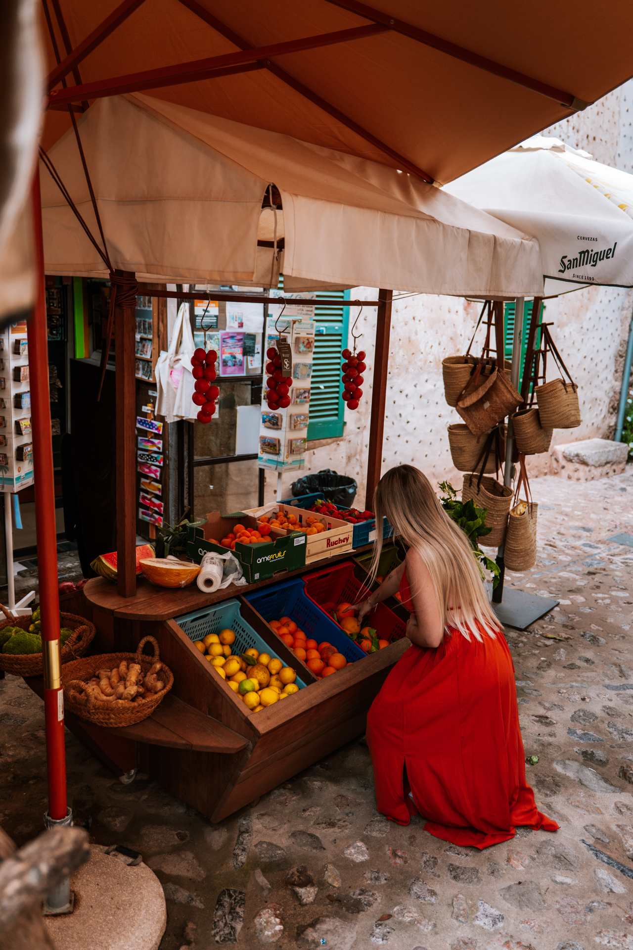 Woman in a red dress shopping at a small fruit stand in the streets of Deià, Mallorca, Spain