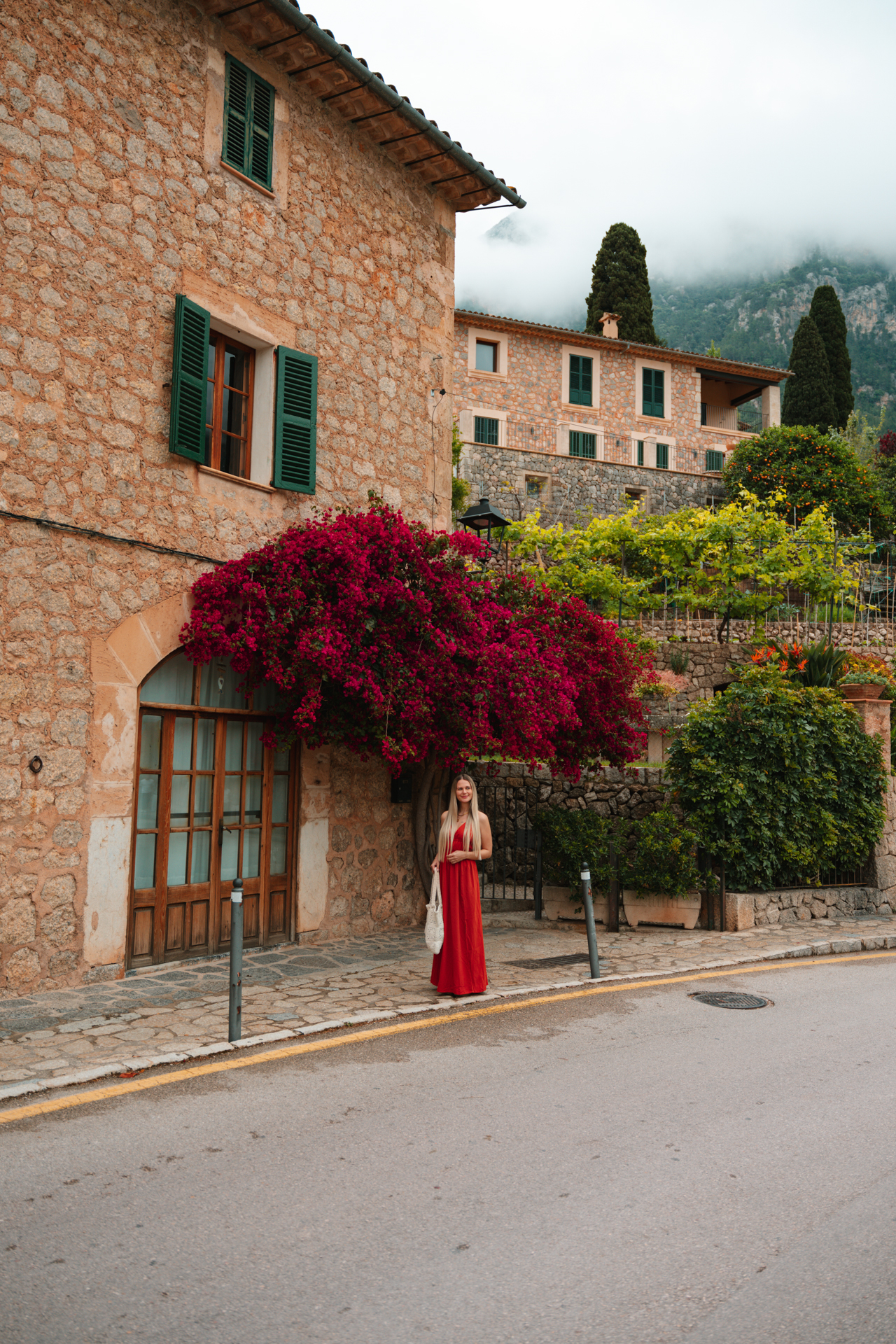 Woman in a red dress beneath vibrant bougainvillea in Deià village, Mallorca, Spain