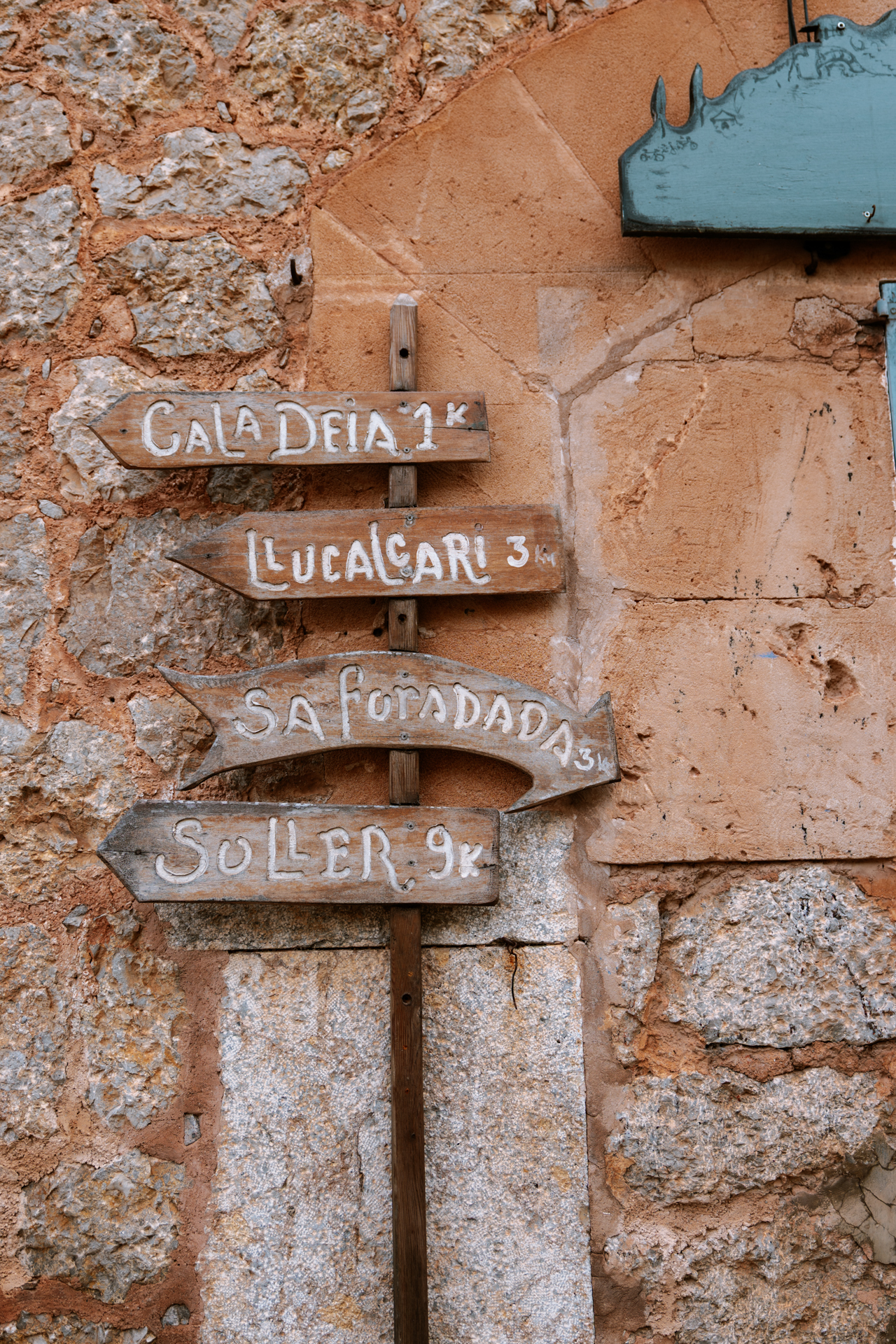 Rustic wooden signpost in Deià pointing toward Cala Deià, Llucalcari, Sa Foradada, and Sóller, Mallorca, Spain