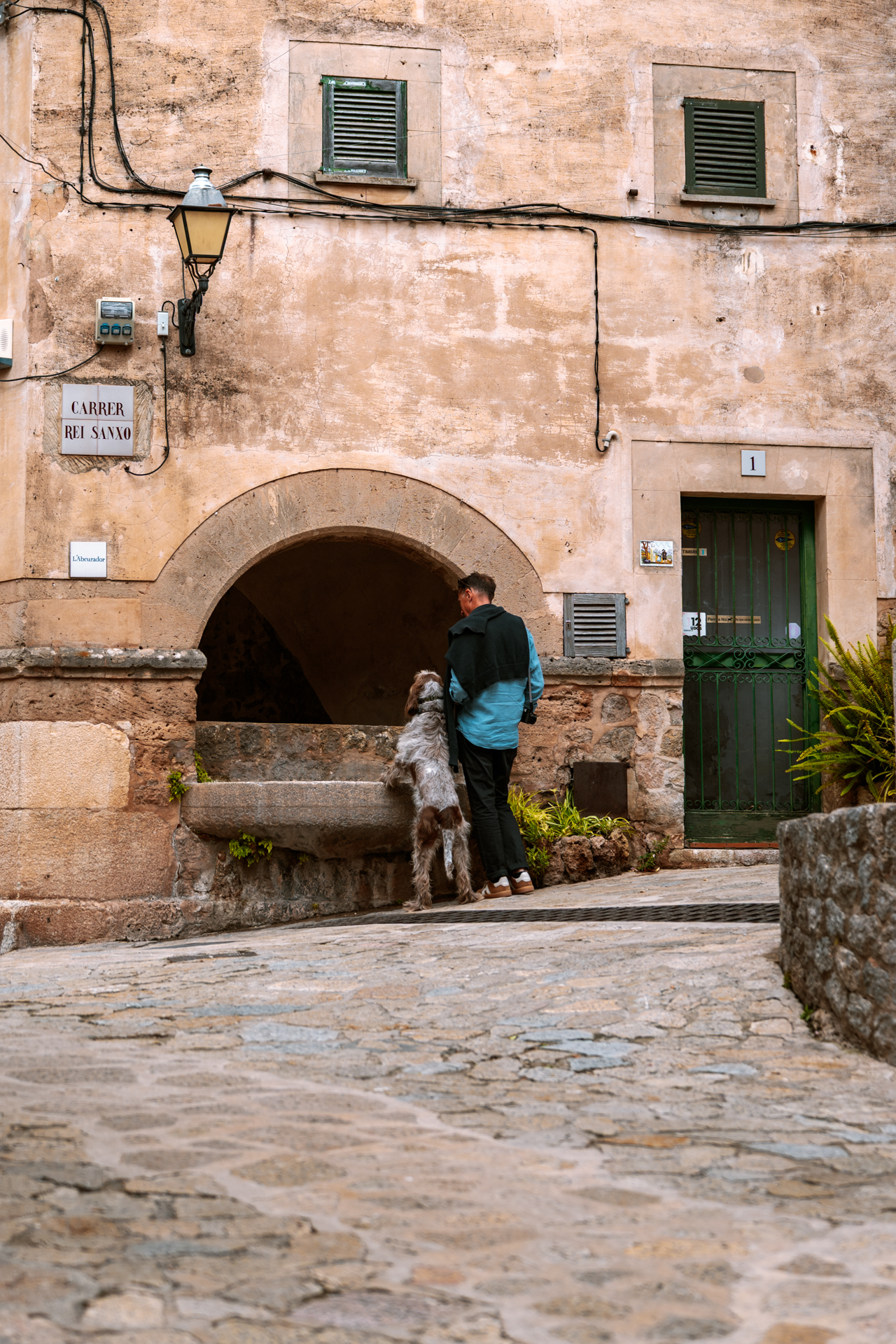 Man with a dog beside a historic stone fountain in Valldemossa, Mallorca, Spain