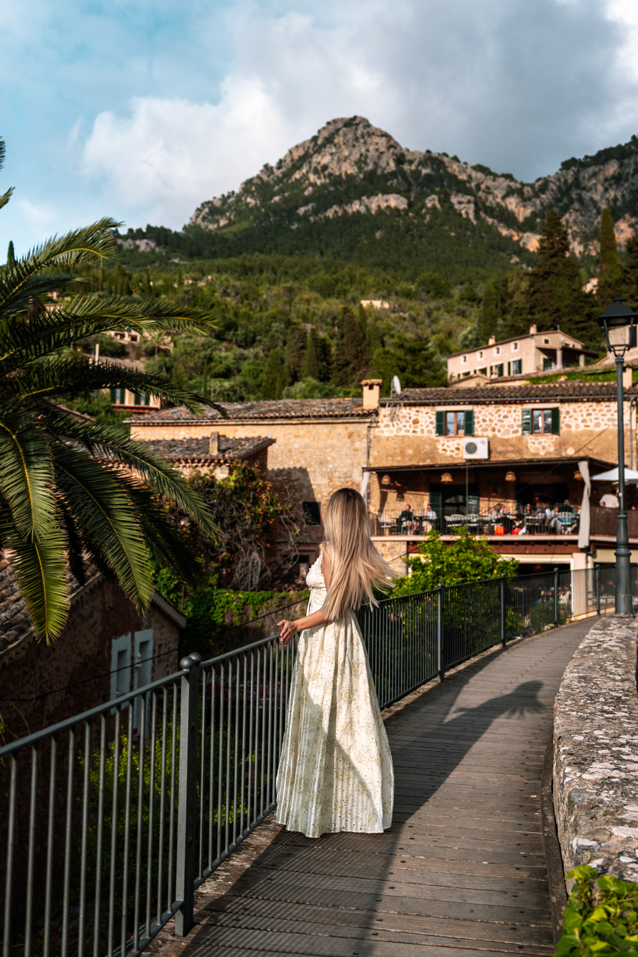 Woman in flowing white dress overlooking the mountain village of Deià, Mallorca, during golden hour