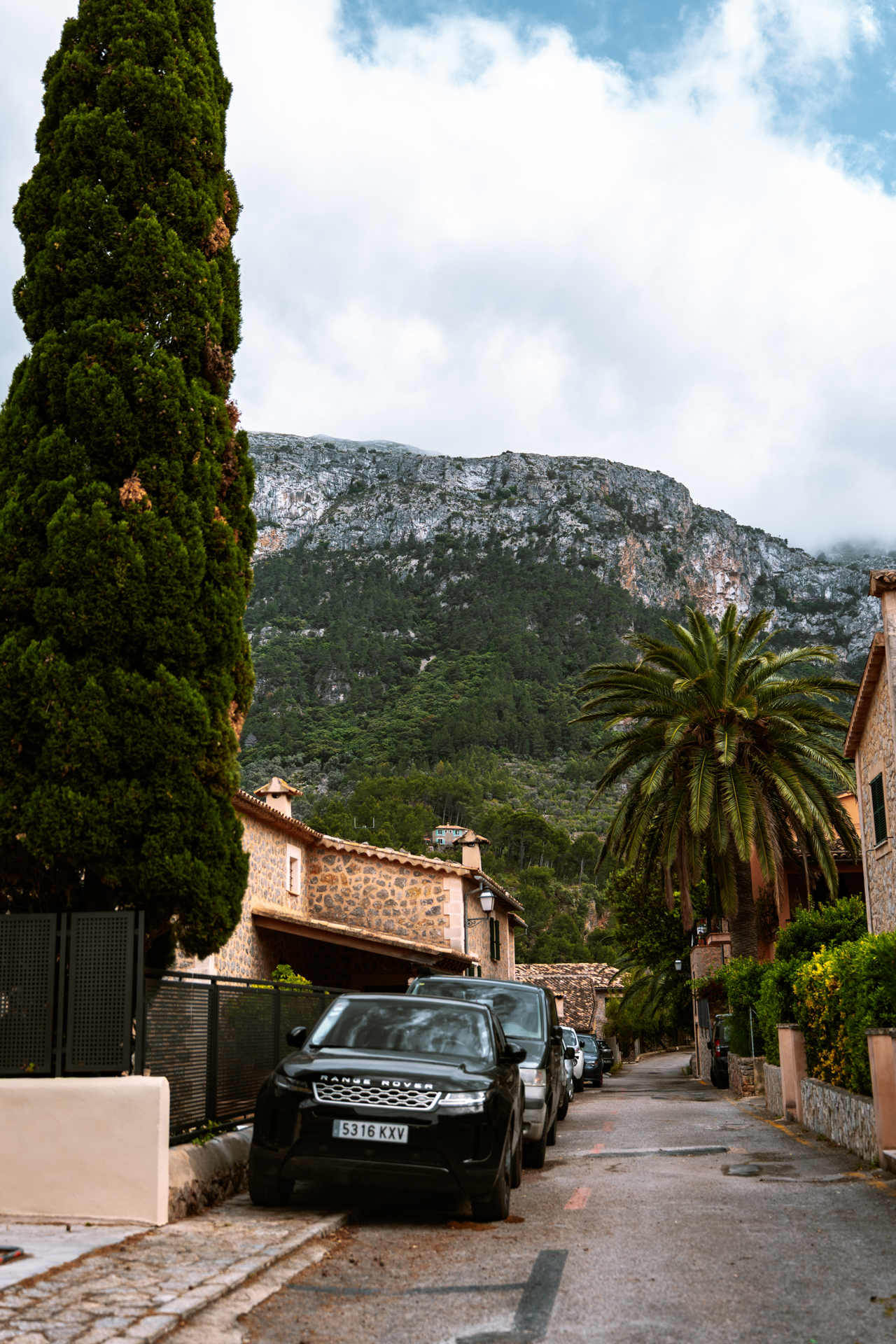 Mountain street in Deià, Mallorca, with stone houses, palm trees, and dramatic Tramuntana mountain backdrop