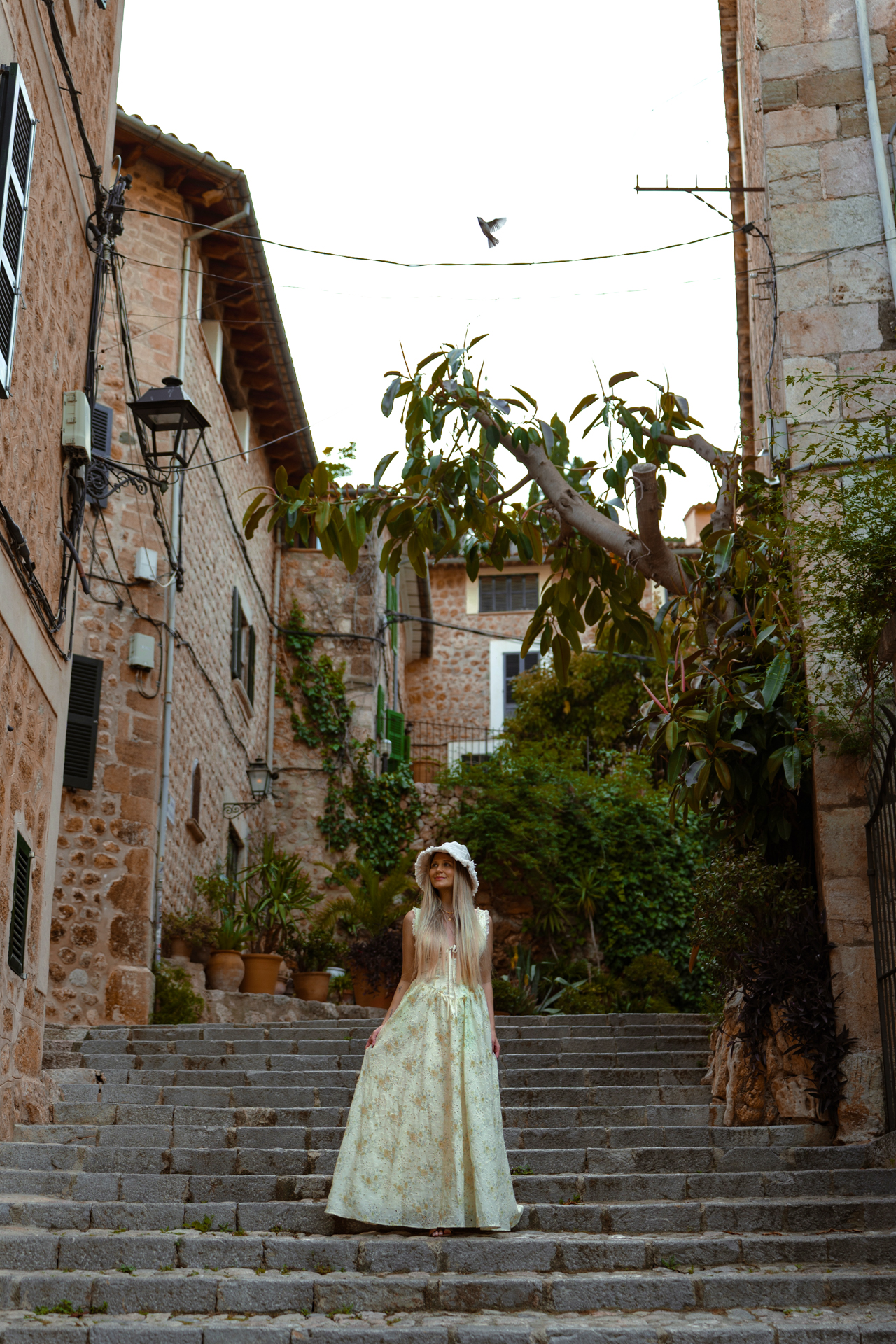Woman in a long dress standing on stone steps in a charming old village in Mallorca, Spain.