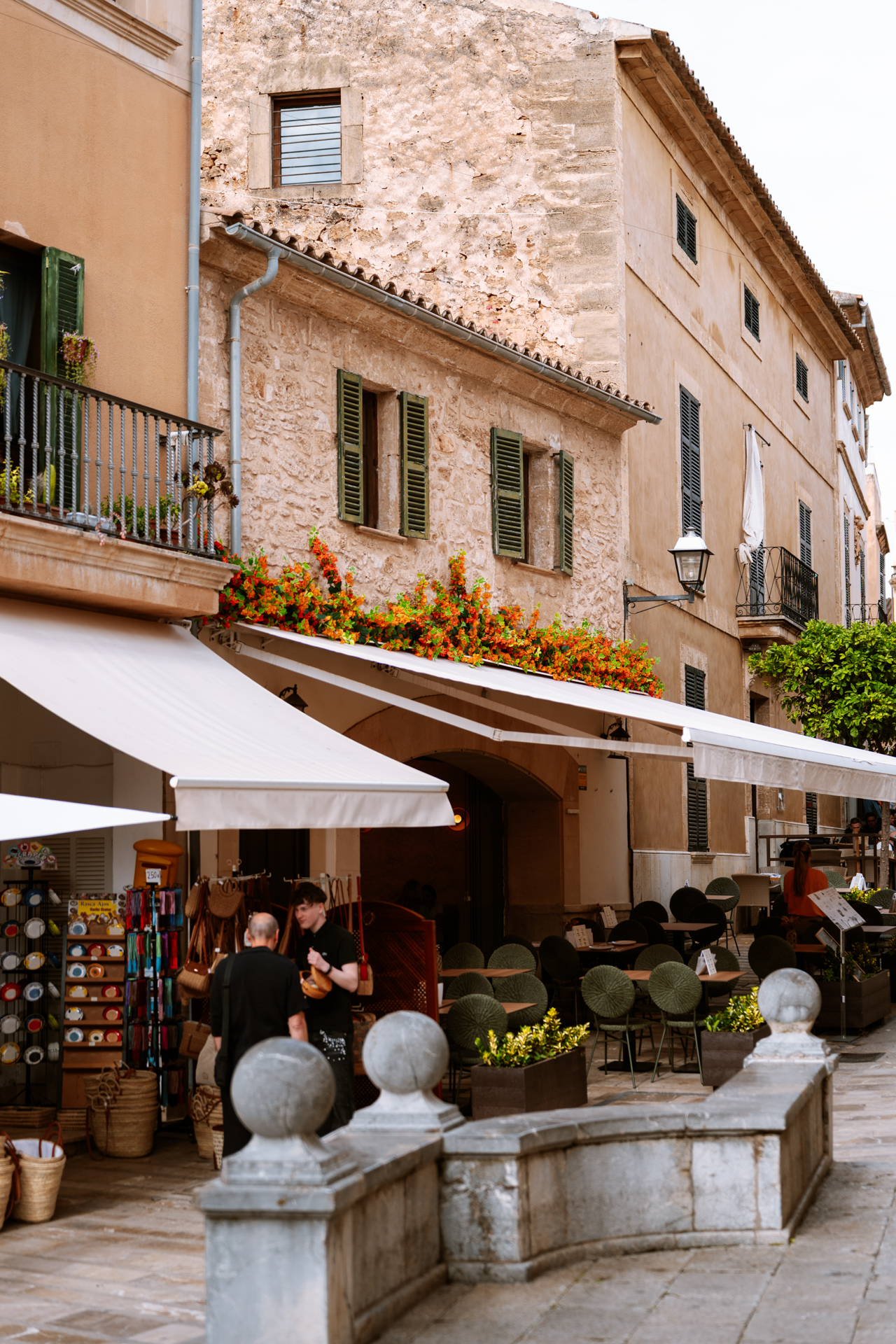 Charming shops and café terraces along a stone street in Alcúdia Old Town, Mallorca.