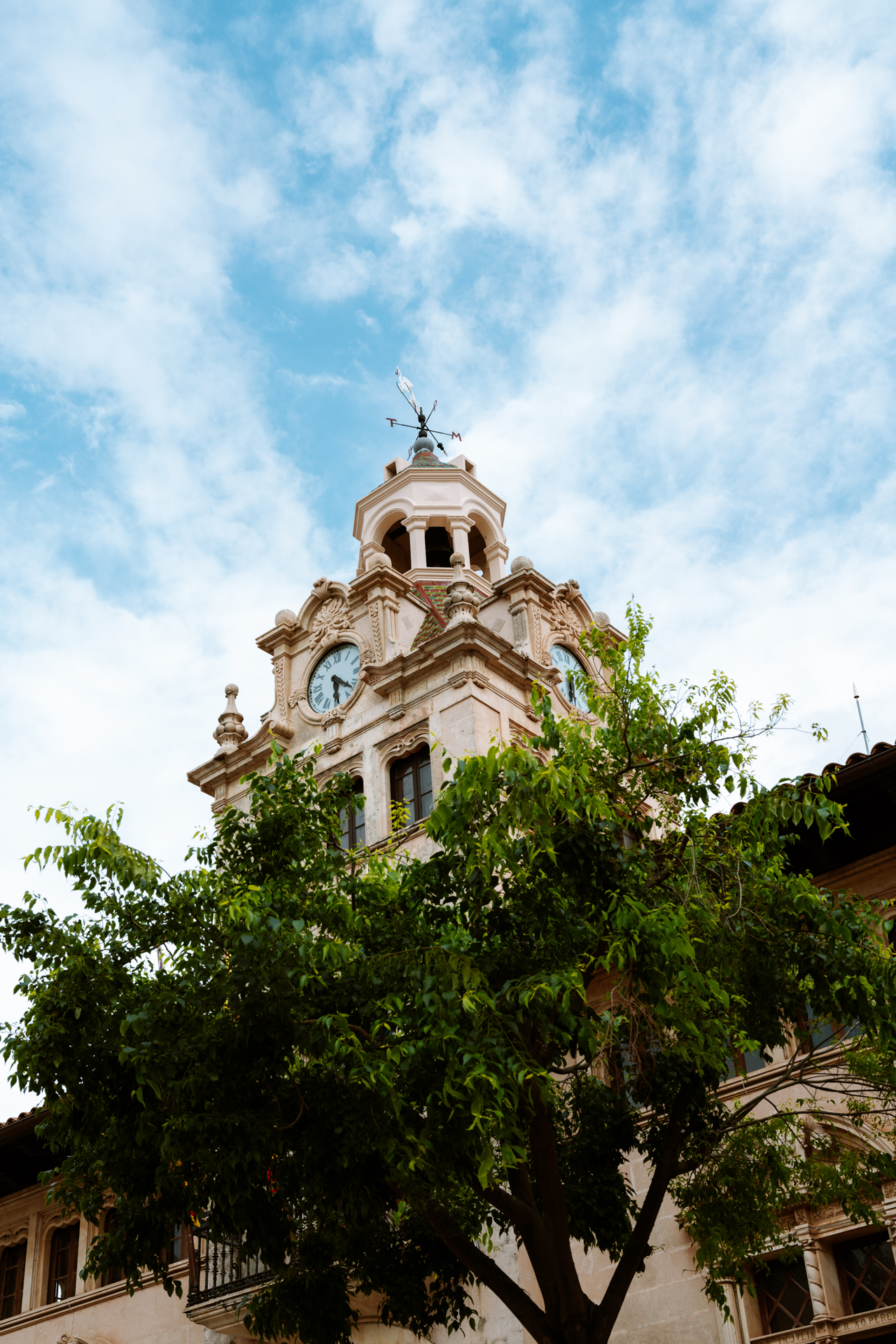 Plaça de la Constitució in Alcúdia Old Town with cafés, historic stone buildings, and the town hall clock tower.