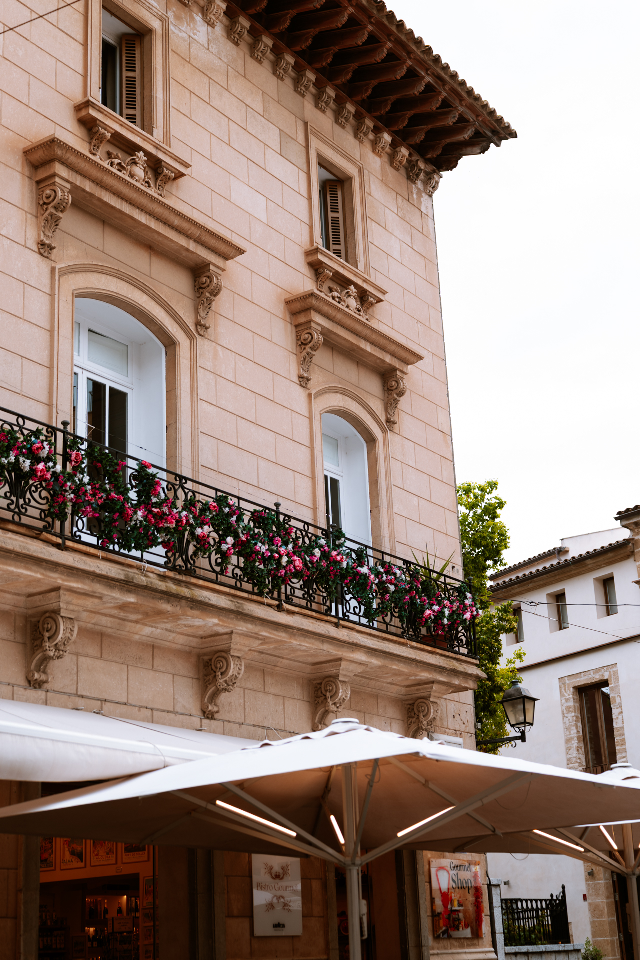 Flower-covered balcony above outdoor cafés in Alcúdia Old Town, Mallorca.
