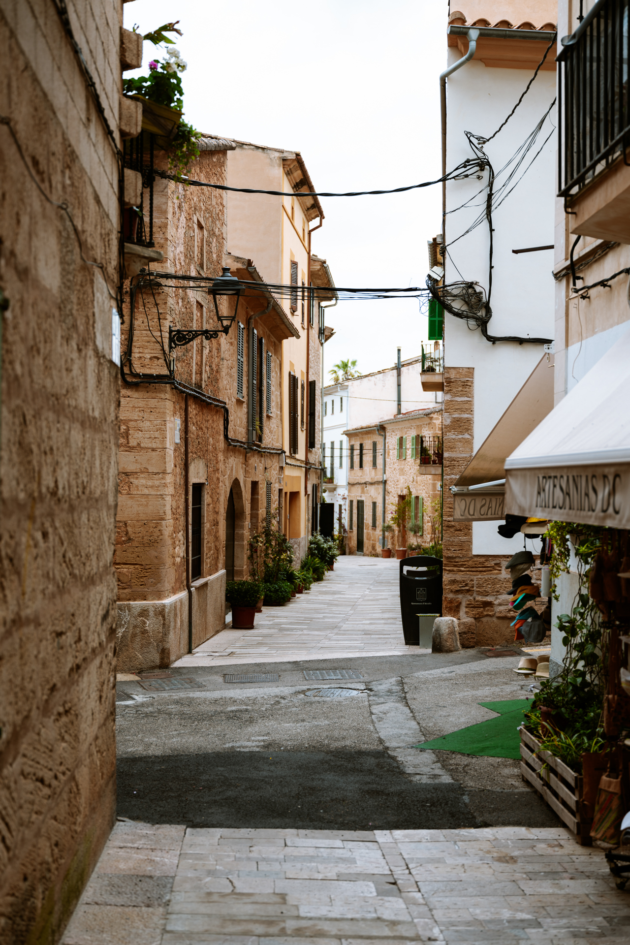 Narrow historic street with stone houses and small shops in Alcúdia Old Town, Mallorca.