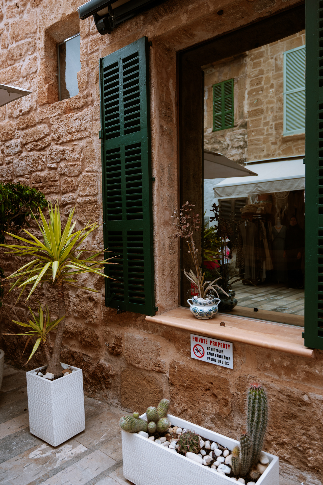 Green shutters, stone walls, and potted plants on a charming street in Alcúdia Old Town.