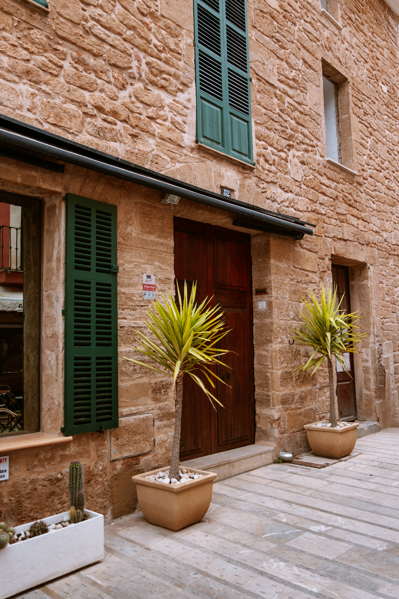 Stone house with green shutters and potted plants in Alcúdia Old Town.