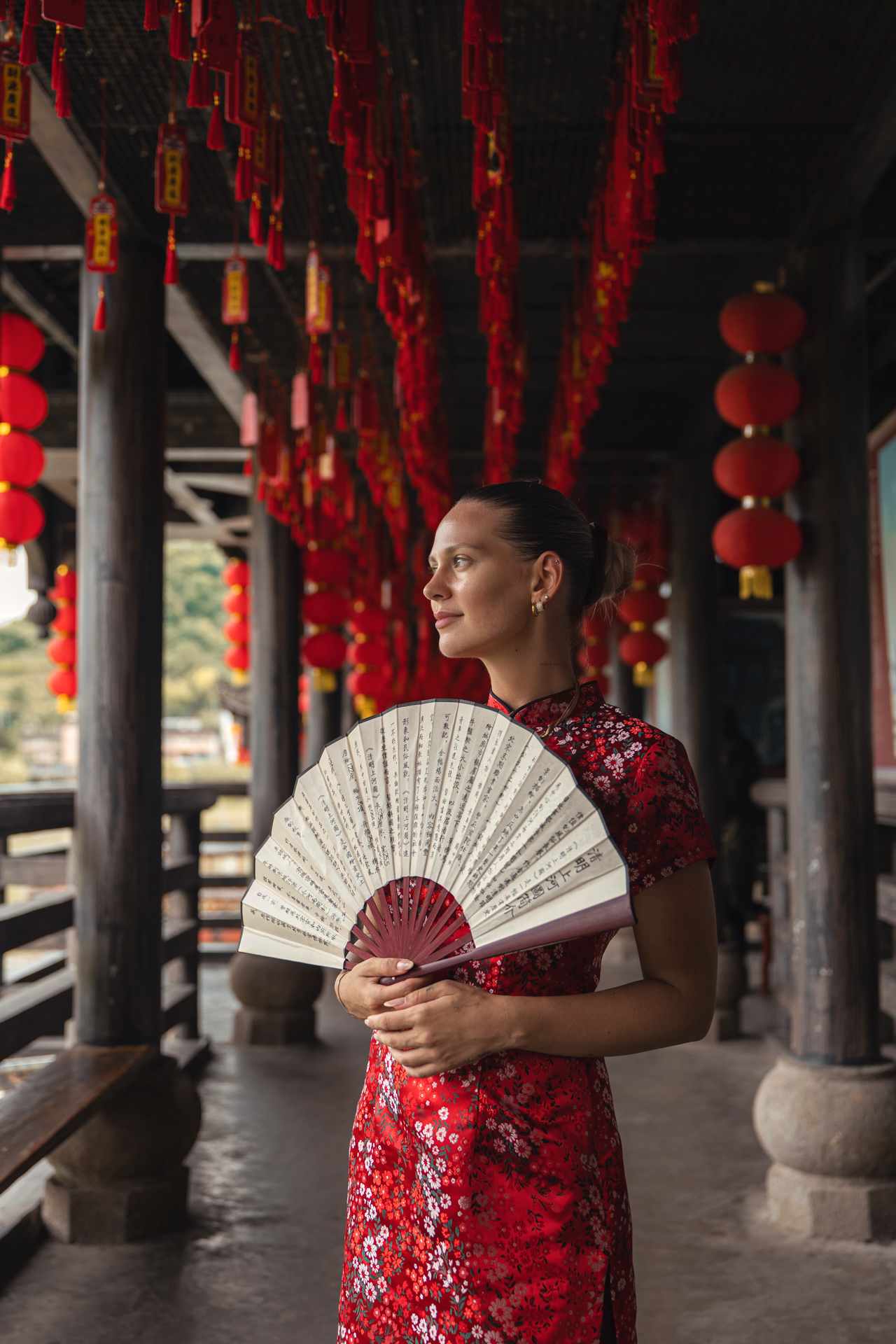 Woman in a red traditional dress holding a Chinese fan in Furong Ancient Town, China.