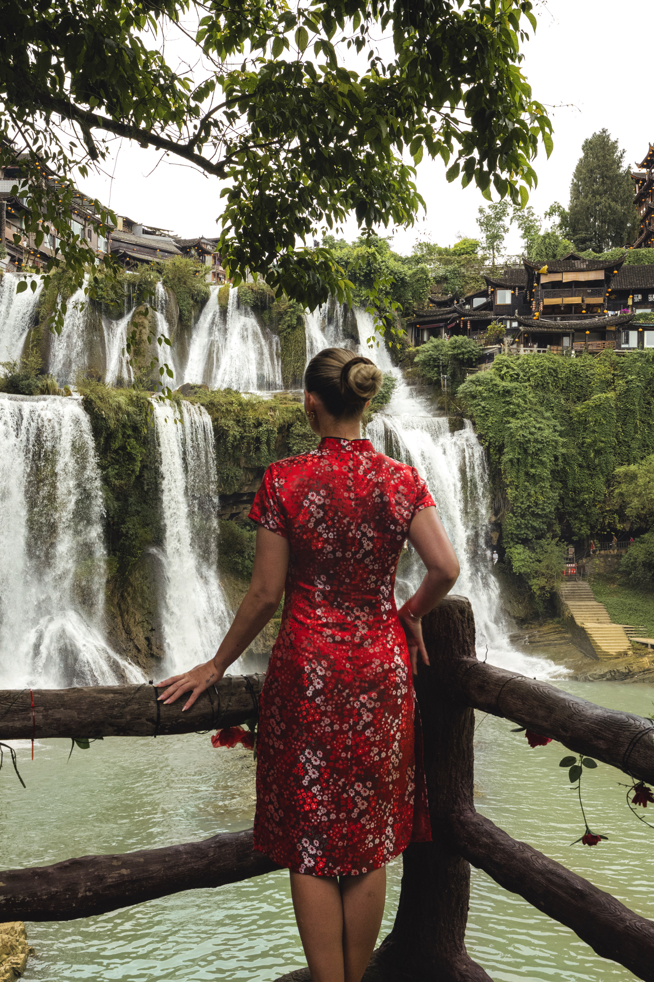 Woman in a red dress overlooking the waterfalls of Furong Ancient Town, China.