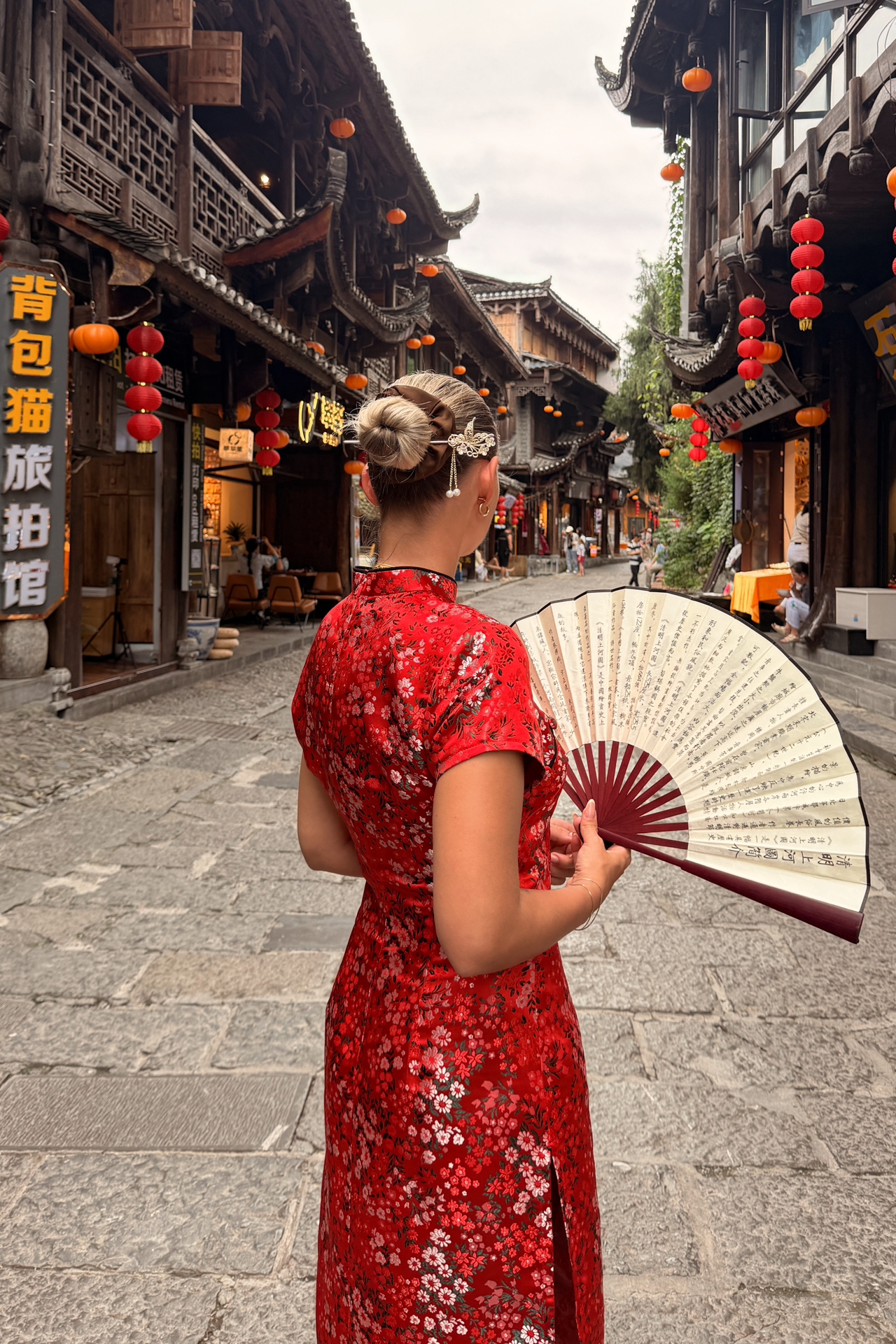 Woman in a red dress holding a Chinese fan on a traditional street in Furong Ancient Town.