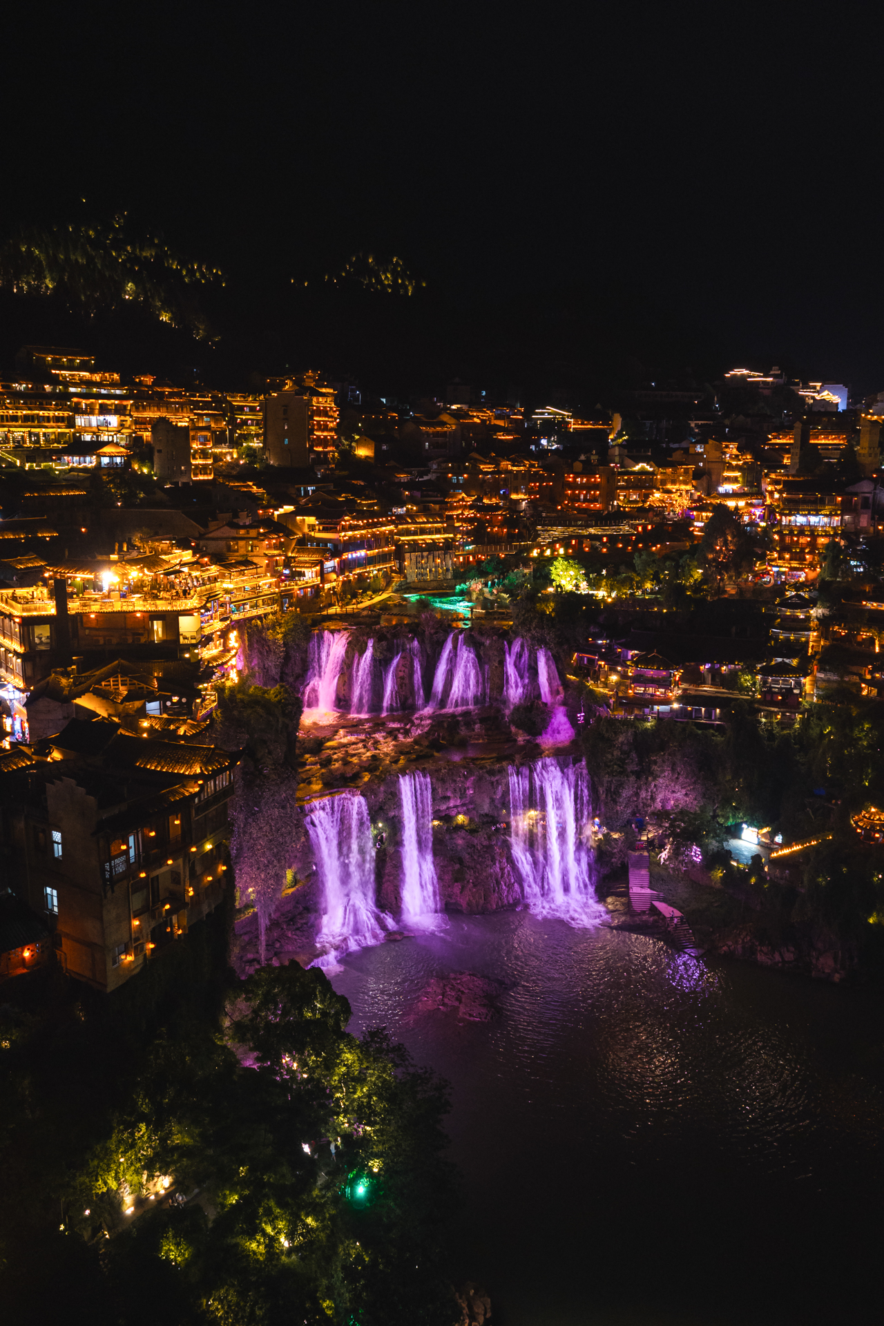 Furong Ancient Town illuminated at night with colorful waterfalls in Hunan, China.