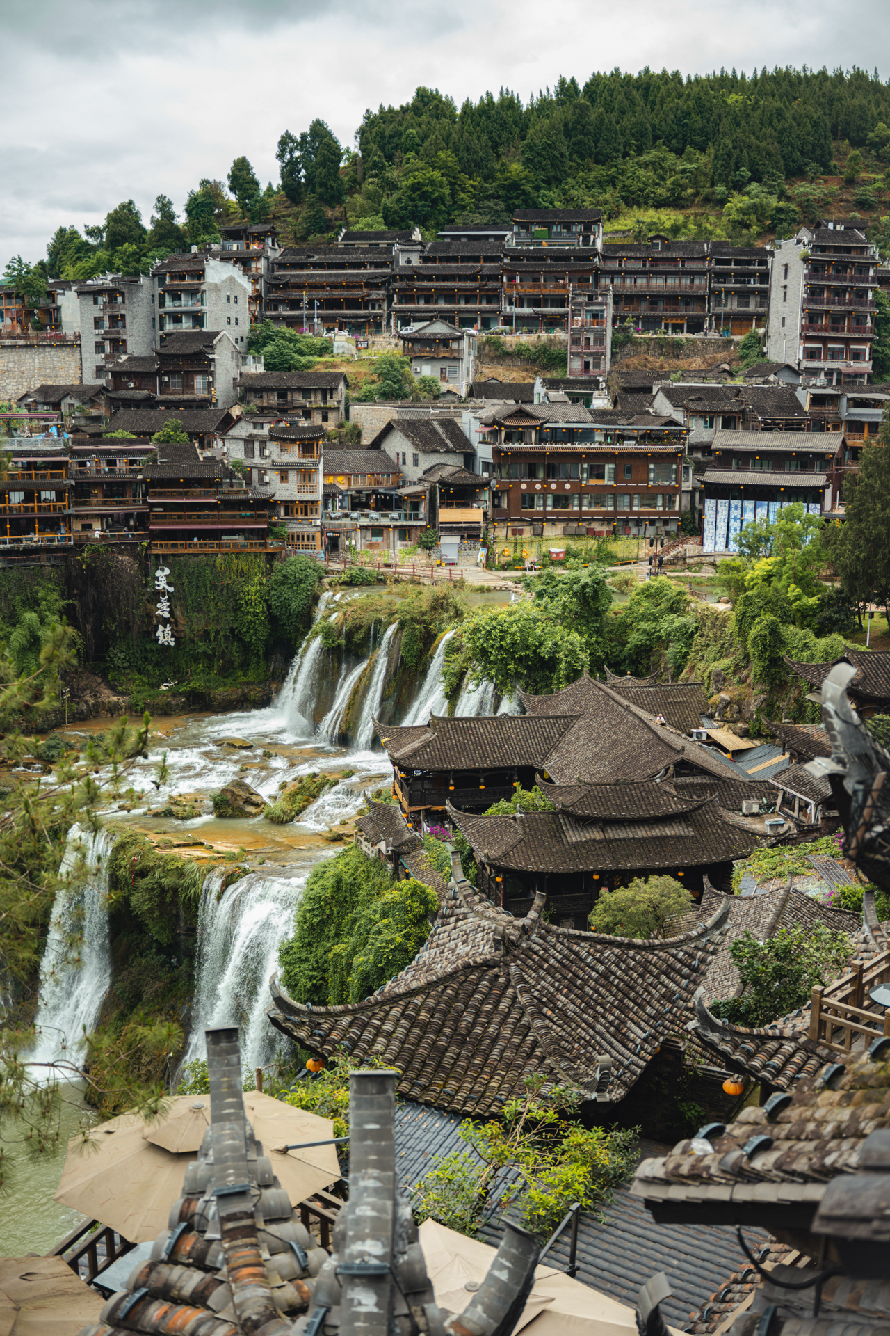 Panoramic view of Furong Ancient Town with waterfalls and traditional rooftops in Hunan, China.