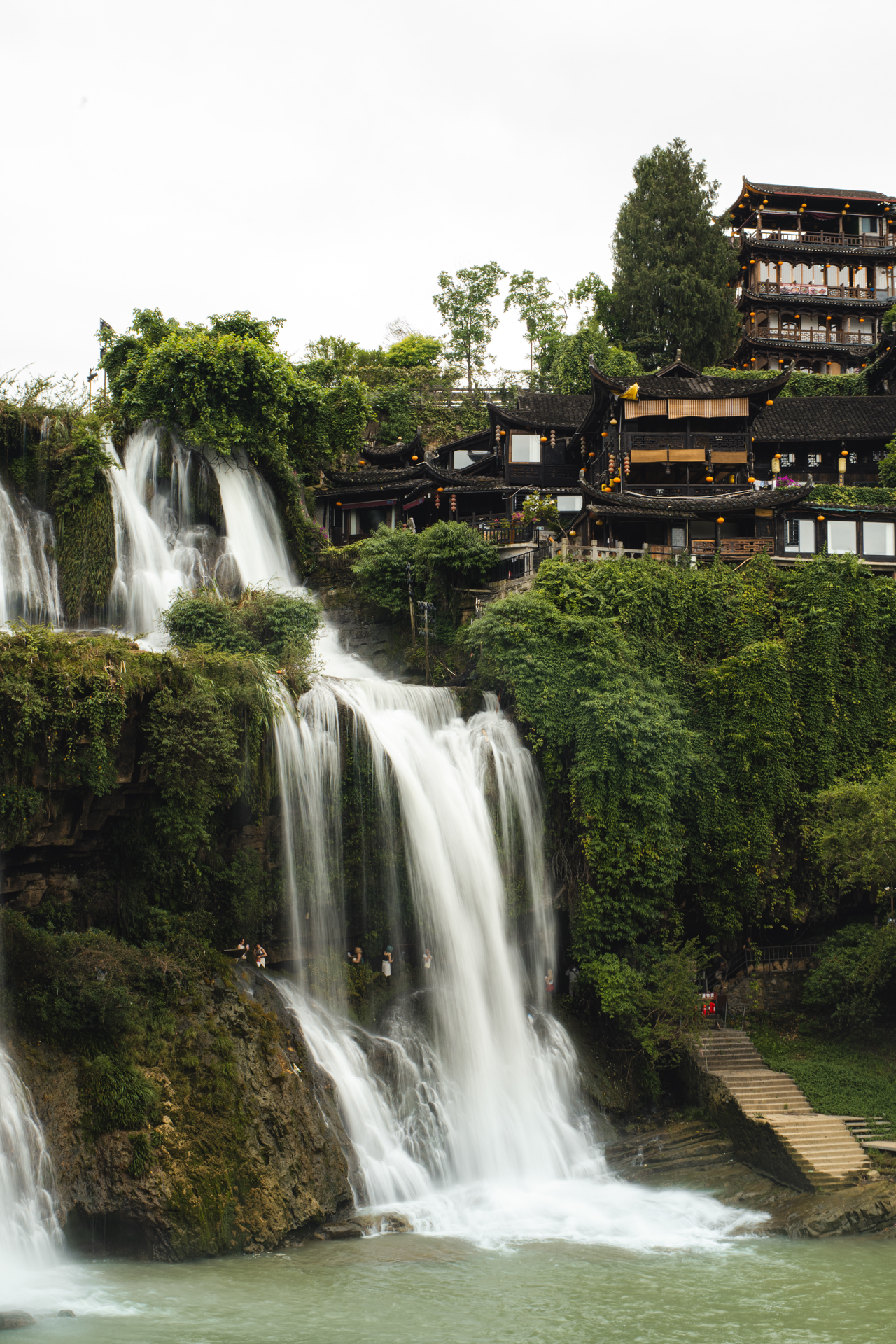 Furong Ancient Town waterfall beside traditional wooden buildings in Hunan, China.